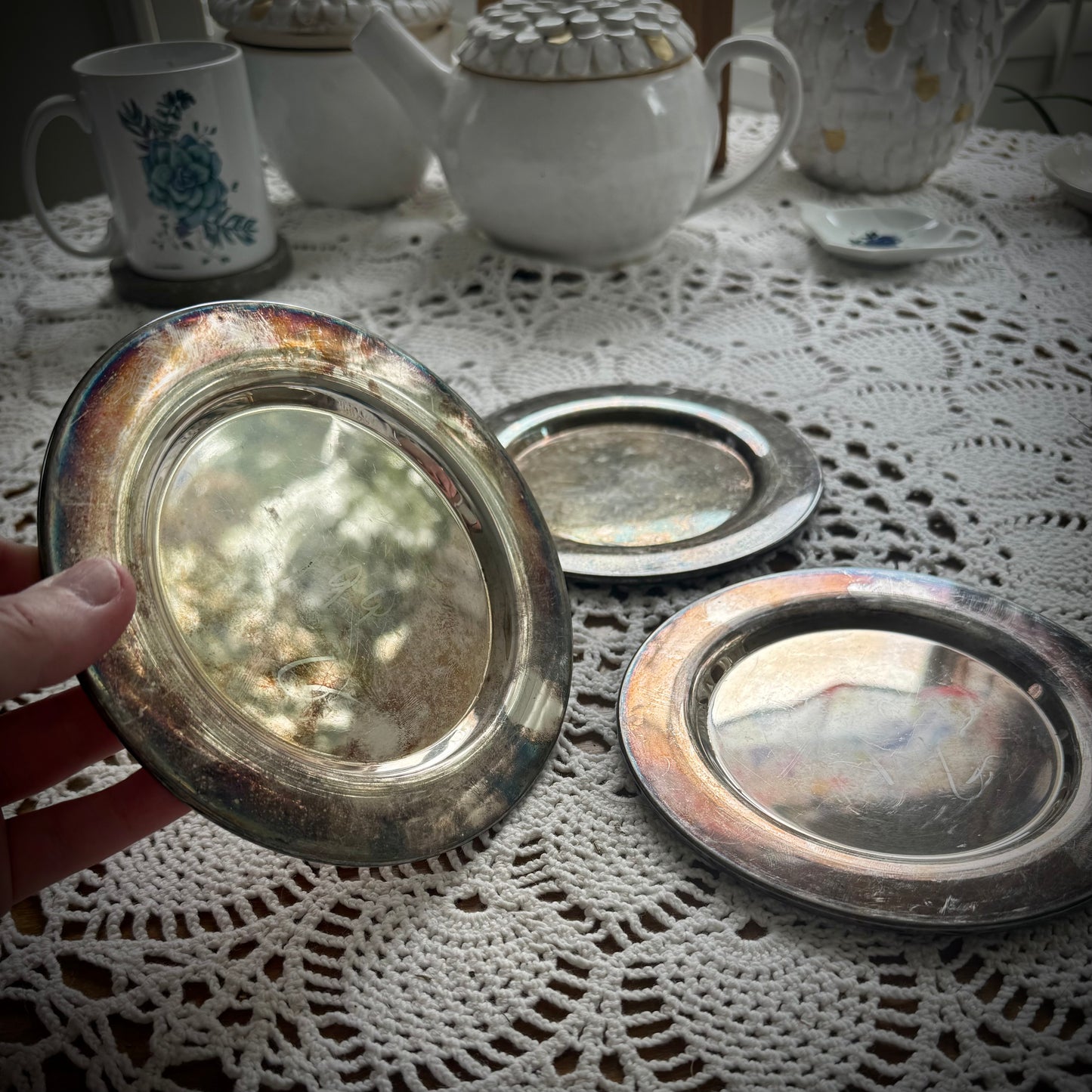 Three round silverplate Offering Plates on a lace surface, reflecting light and showing signs of wear.