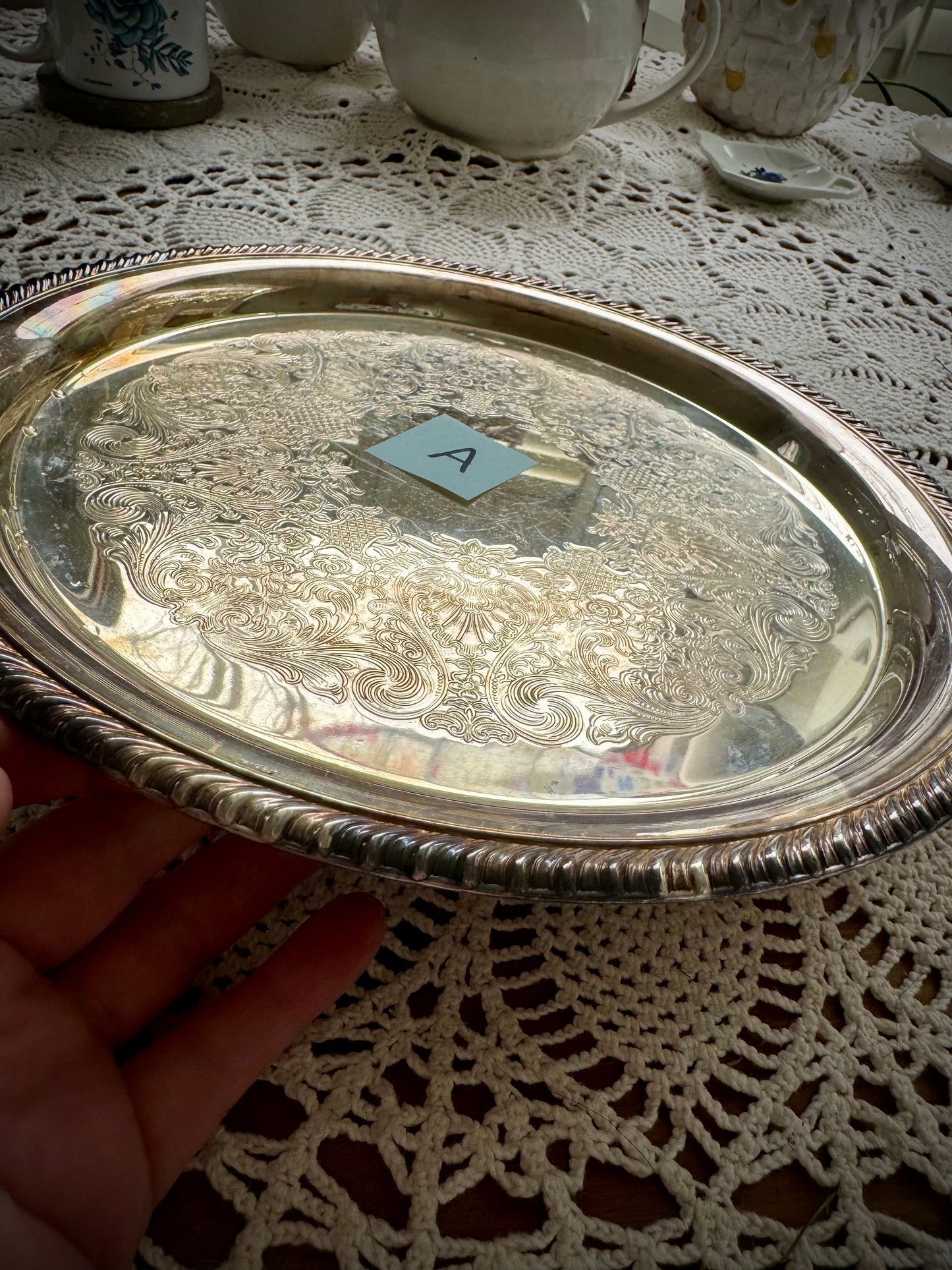 A silverplate round offering tray is displayed on a white lace surface. On the tray is a post-in with the letter "A"