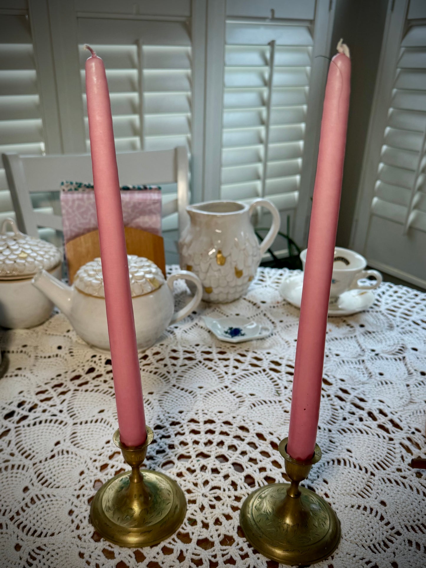 A set of two a vintage brass taper candle holder with etching on the base, holding two tall pink taper candles.