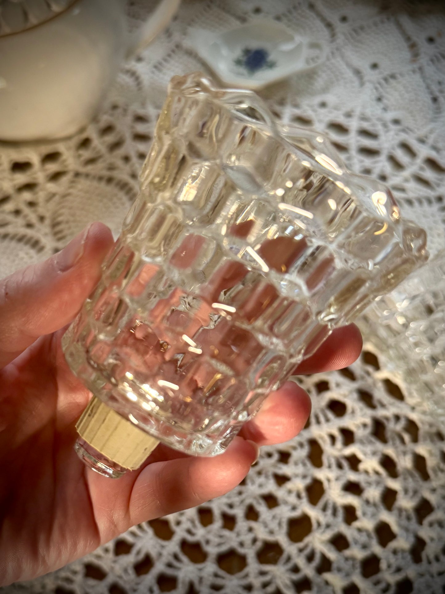 A vintage glass votive candle holder with a peg and gasket bottom being held over a table with a white lace tablecloth