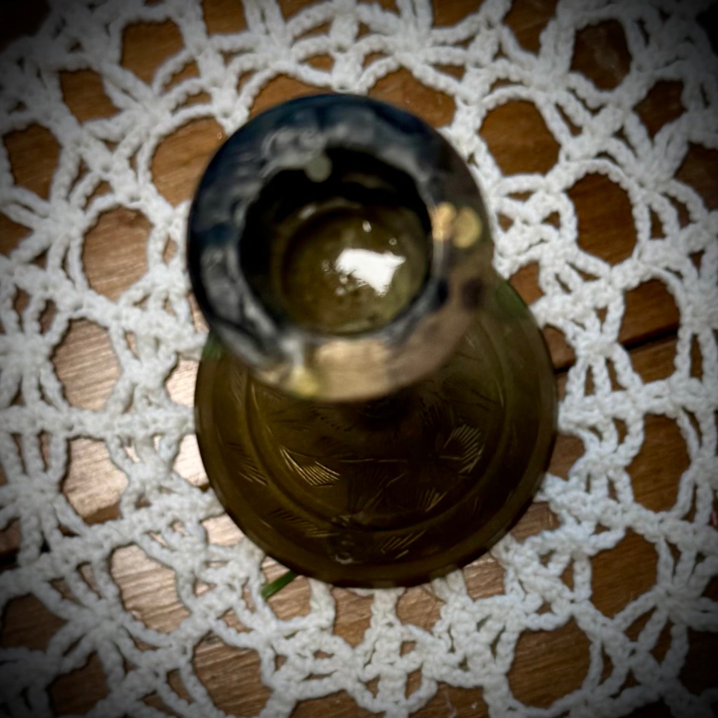 A vintage brass candle holder with etching on the base, displayed on a white lace tablecloth.