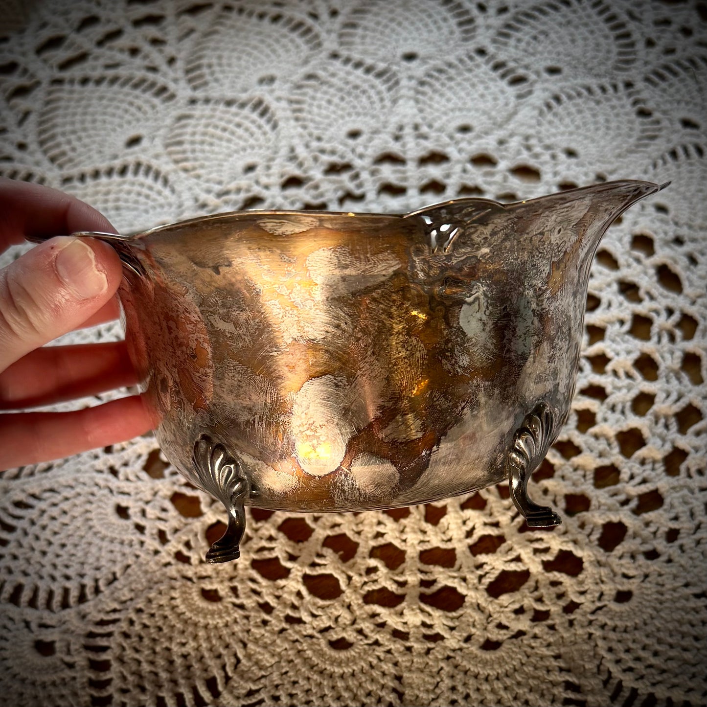 A vintage silver serving bowl with scalloped edges and feet, placed on a table with a lace tablecloth.