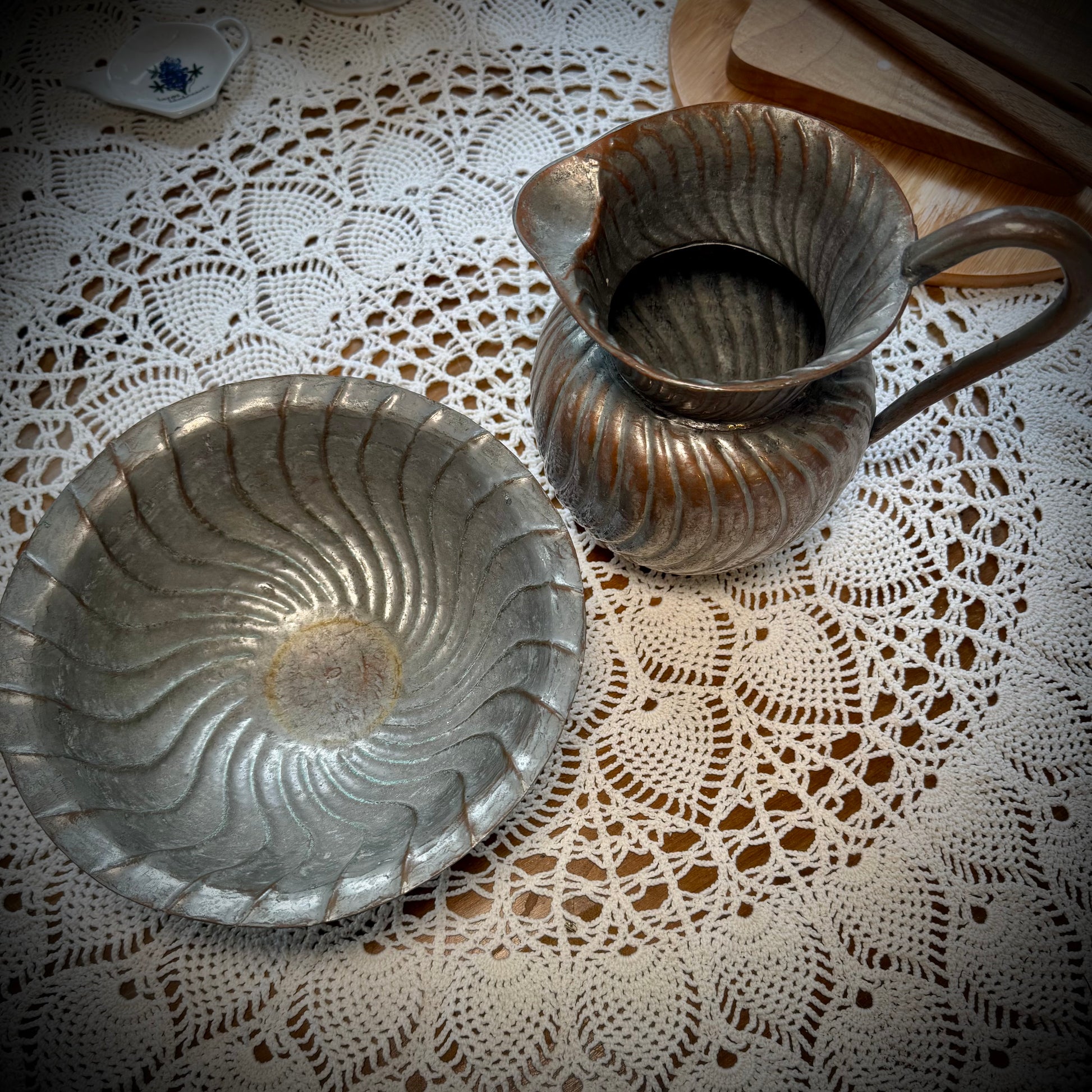 Aerial view of an antique swirl tinned copper pitcher and bowl placed on a table with a lace tablecloth.