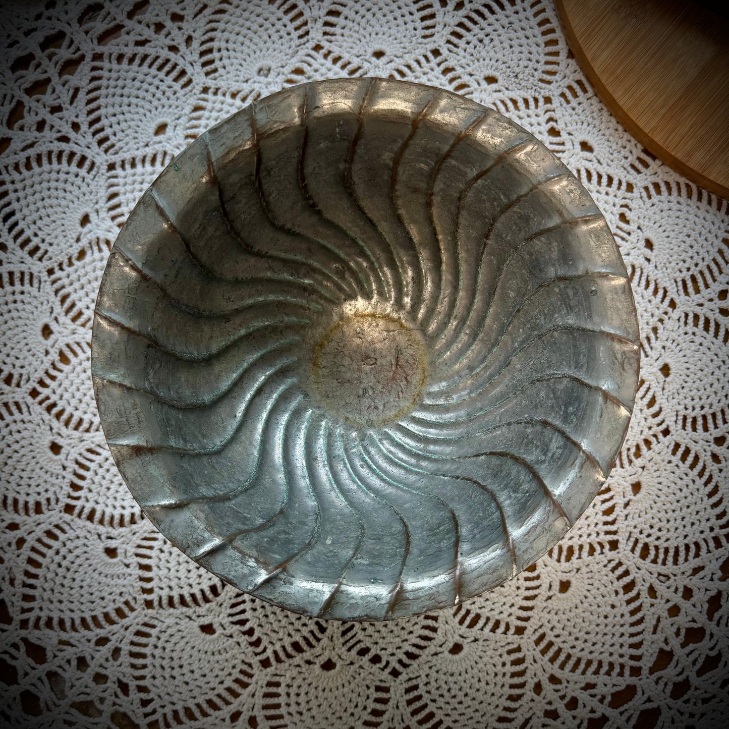 An antique swirl tinned copper bowl placed on a table with a lace tablecloth.