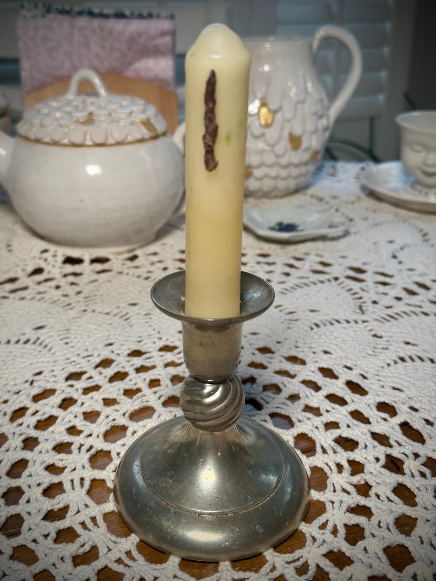 A small pewter candlestick with a small white taper candle