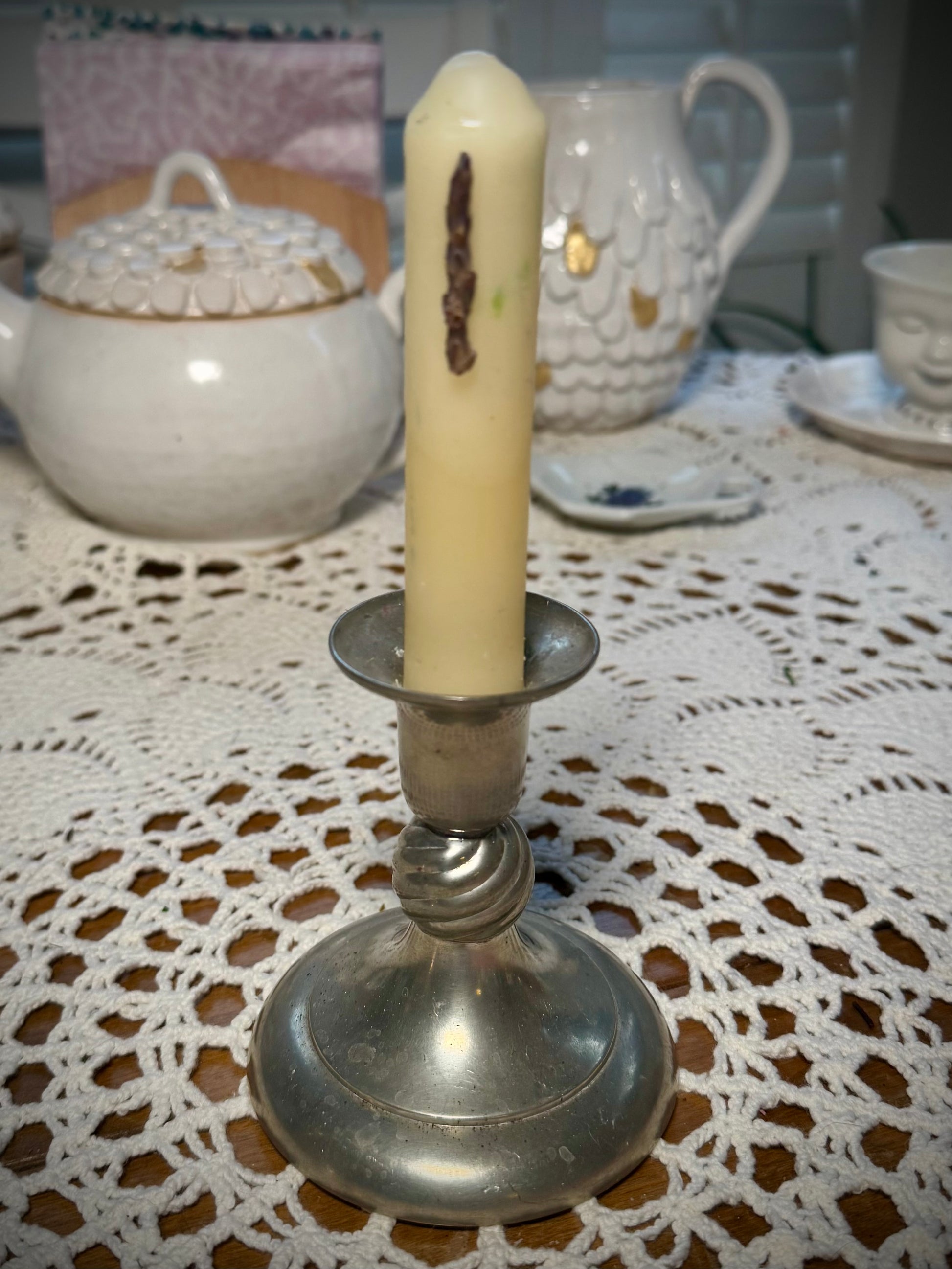 A small pewter candlestick with a small white taper candle