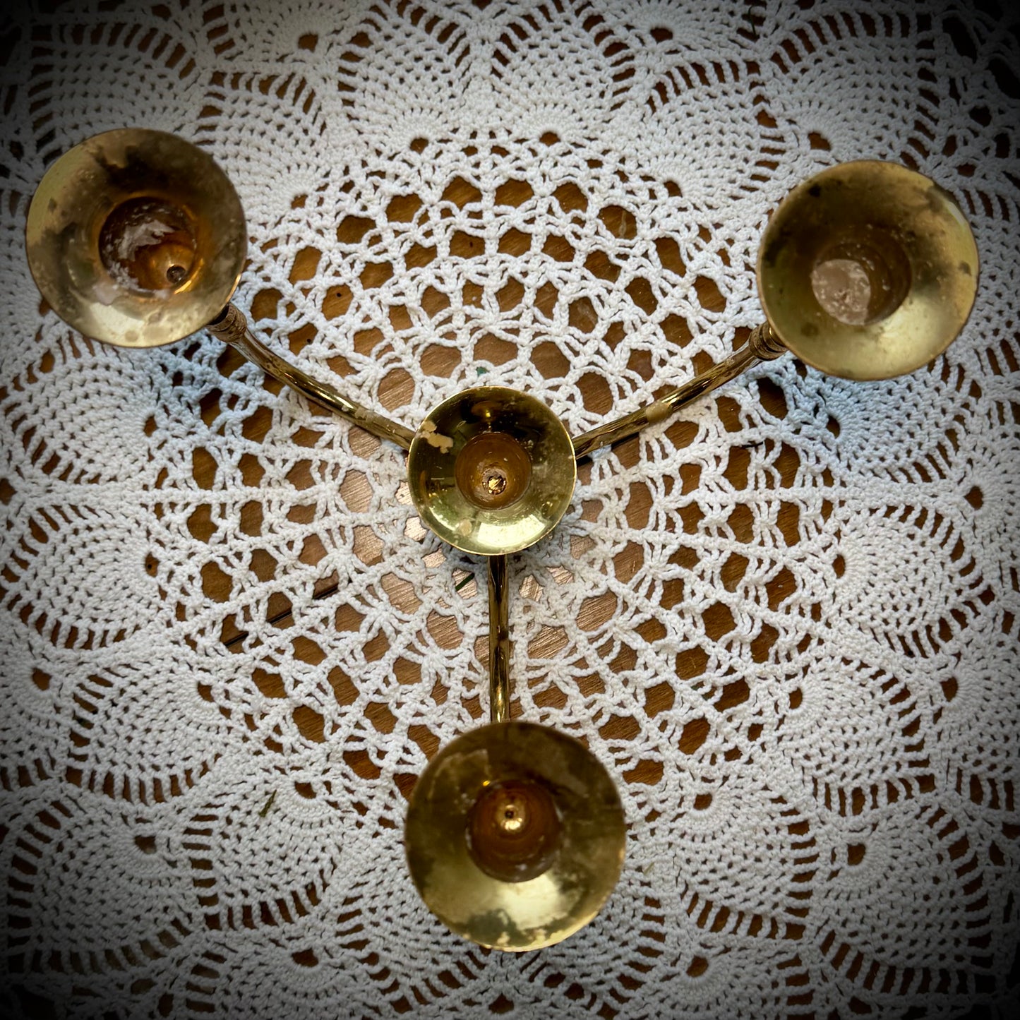A vintage brass four-arm candelabra placed on a table with a lace tablecloth.