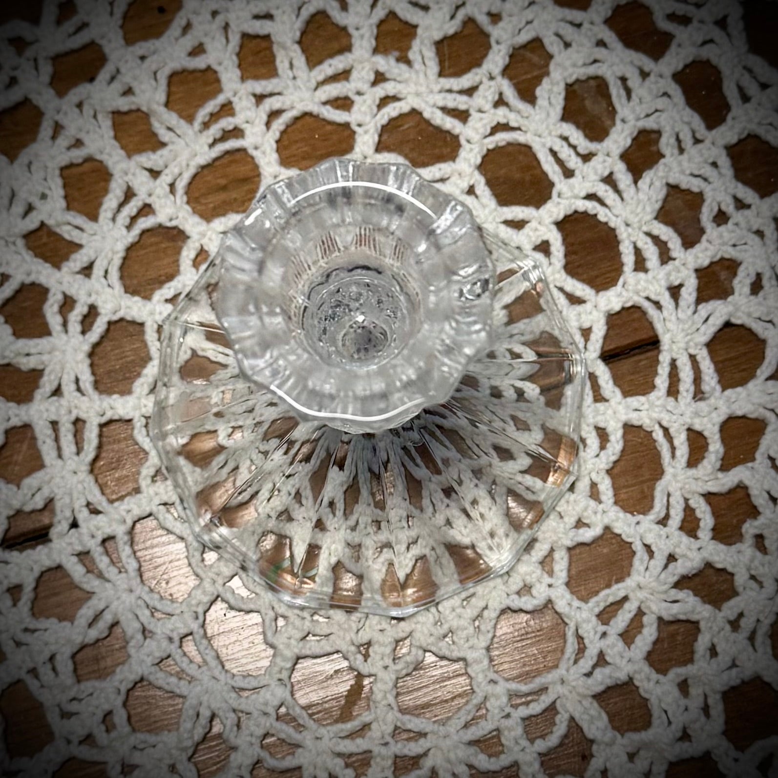 Aerial view of a small vintage clear glass candlestick on a table with a lace tablecloth, designed to hold a taper candle.