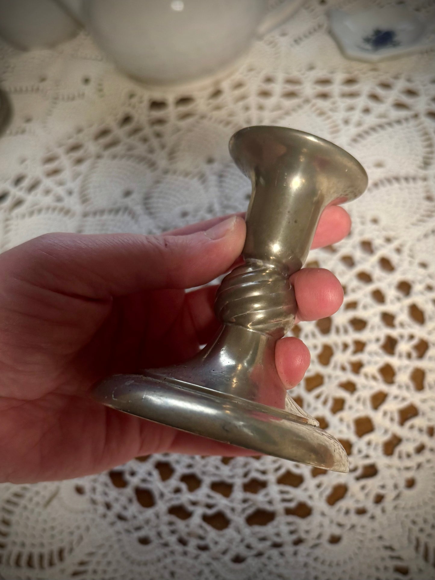 A short vintage pewter candlestick being held over a table with a white lace tablecloth