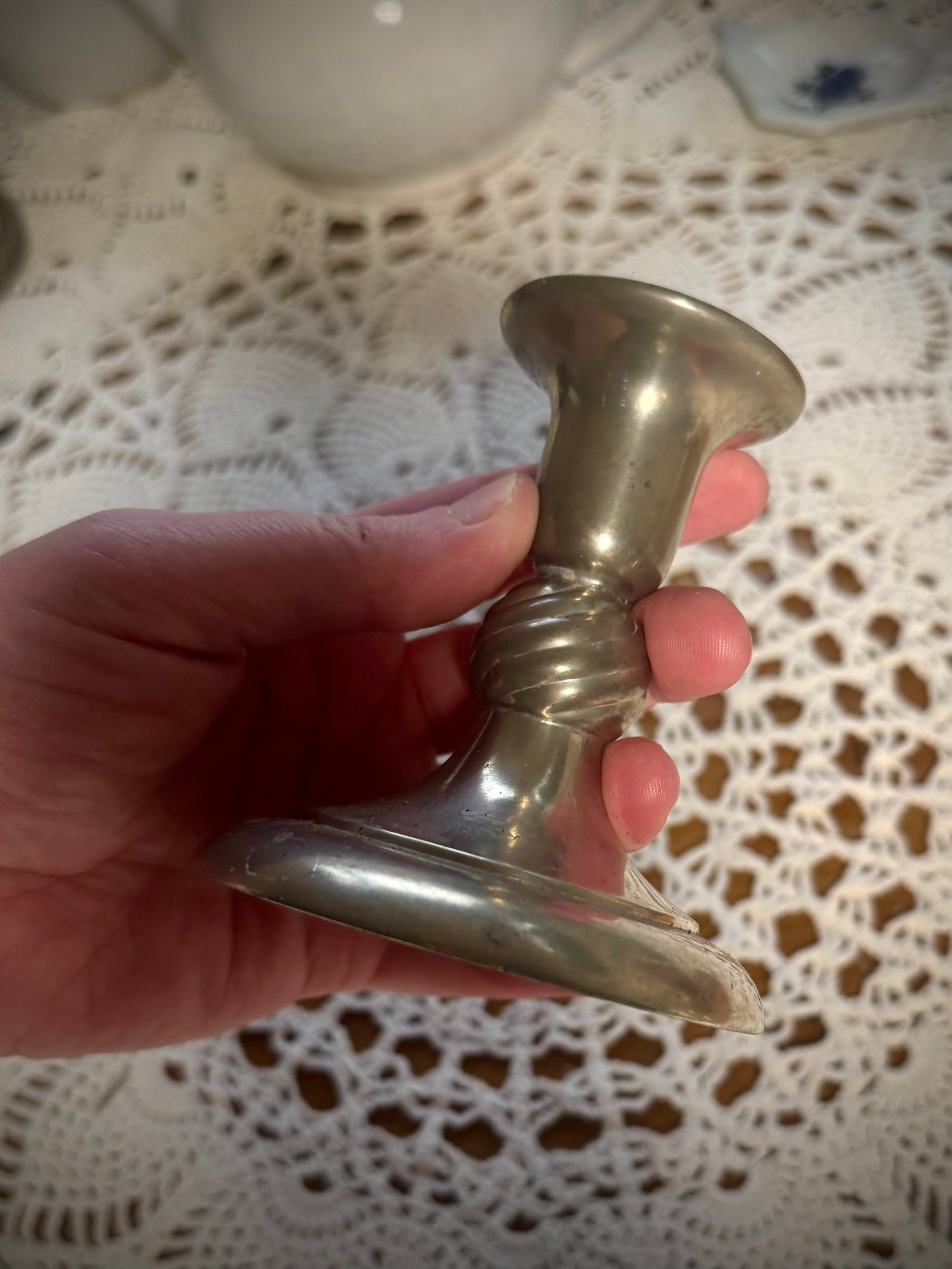 A short vintage pewter candlestick being held over a table with a white lace tablecloth