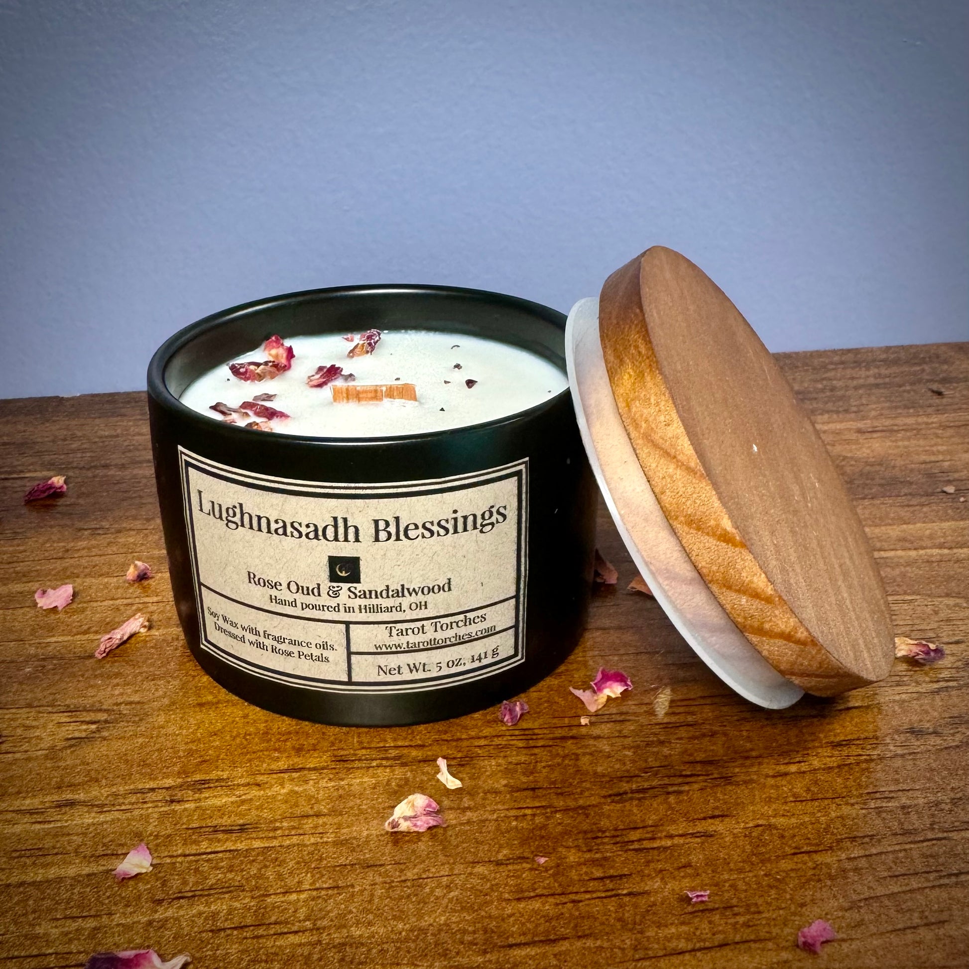 A ceramic candle labeled 'Lughnasadh Blessings' with an offset pine lid placed on a wooden surface against a purple background.