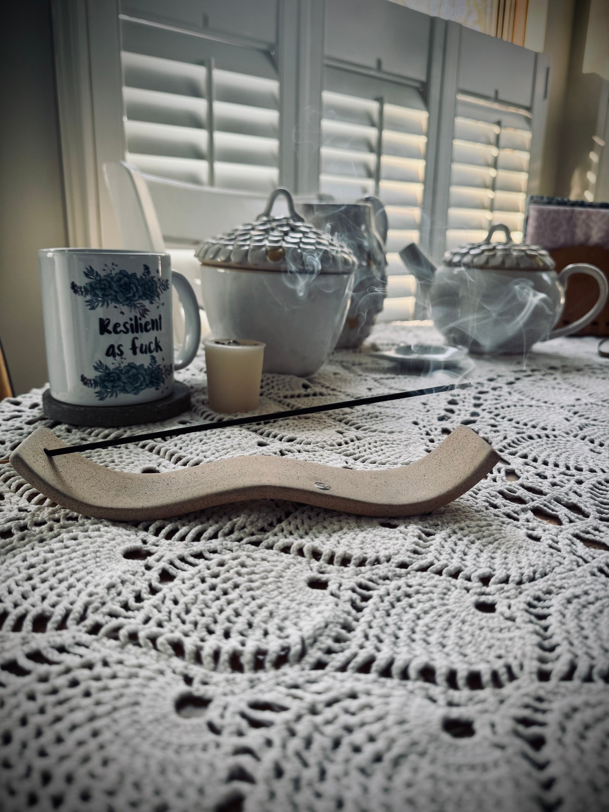 An incense stick burning in a natural colored holder on a white tablecloth