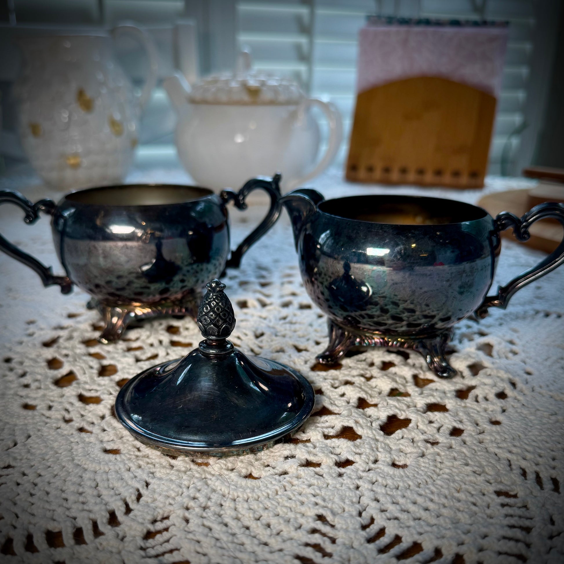 A vintage WM Rogers Silverplate cream and sugar set on a table with a lace tablecloth.