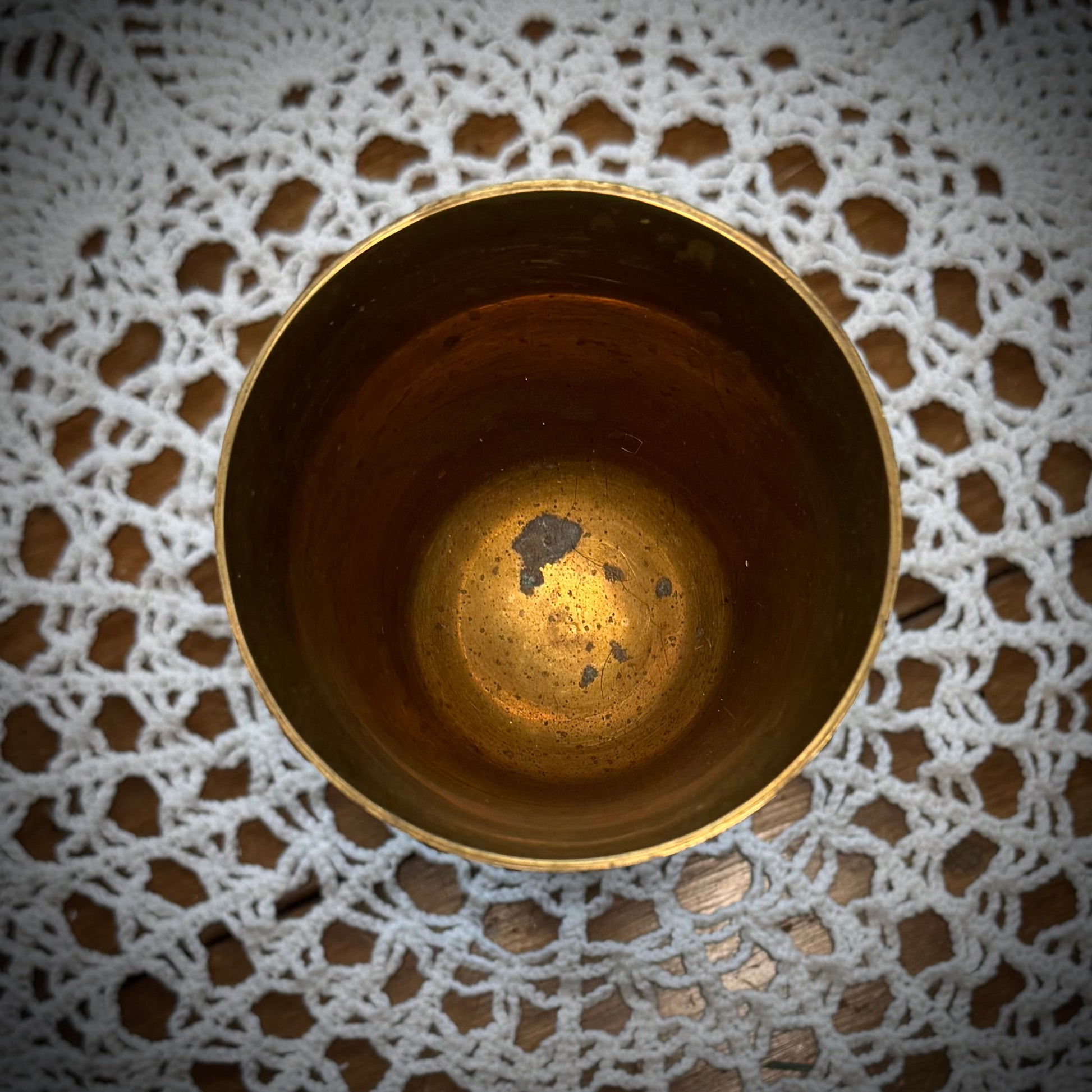 Etched brass colored goblet placed on a table with a white lace tablecloth