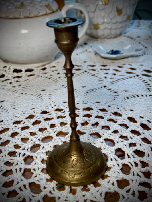 A vintage brass candle holder with etching on the base, displayed on a white lace tablecloth.
