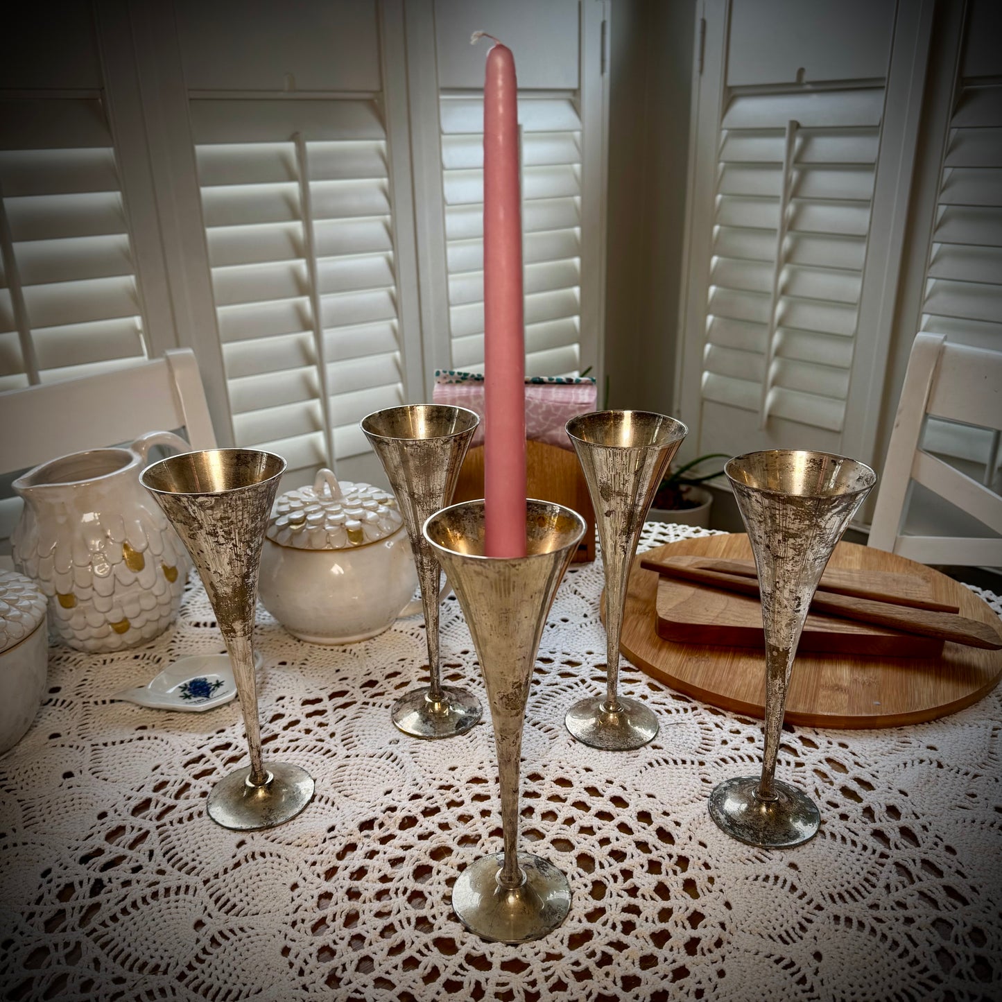 A set of vintage silver plate champagne flutes displayed with a taper candle in the center one