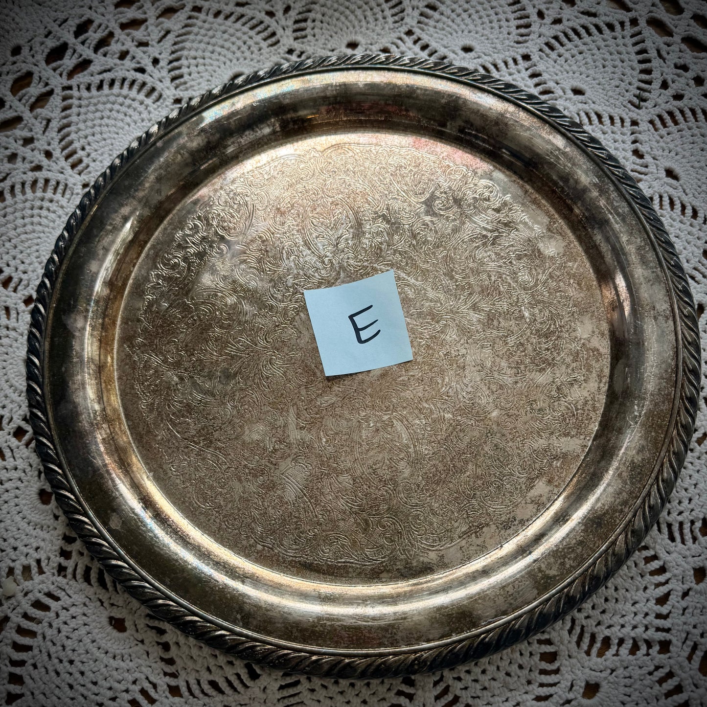 A silverplate round offering tray is displayed on a white lace surface. The tray has a post-it with the letter "E"
