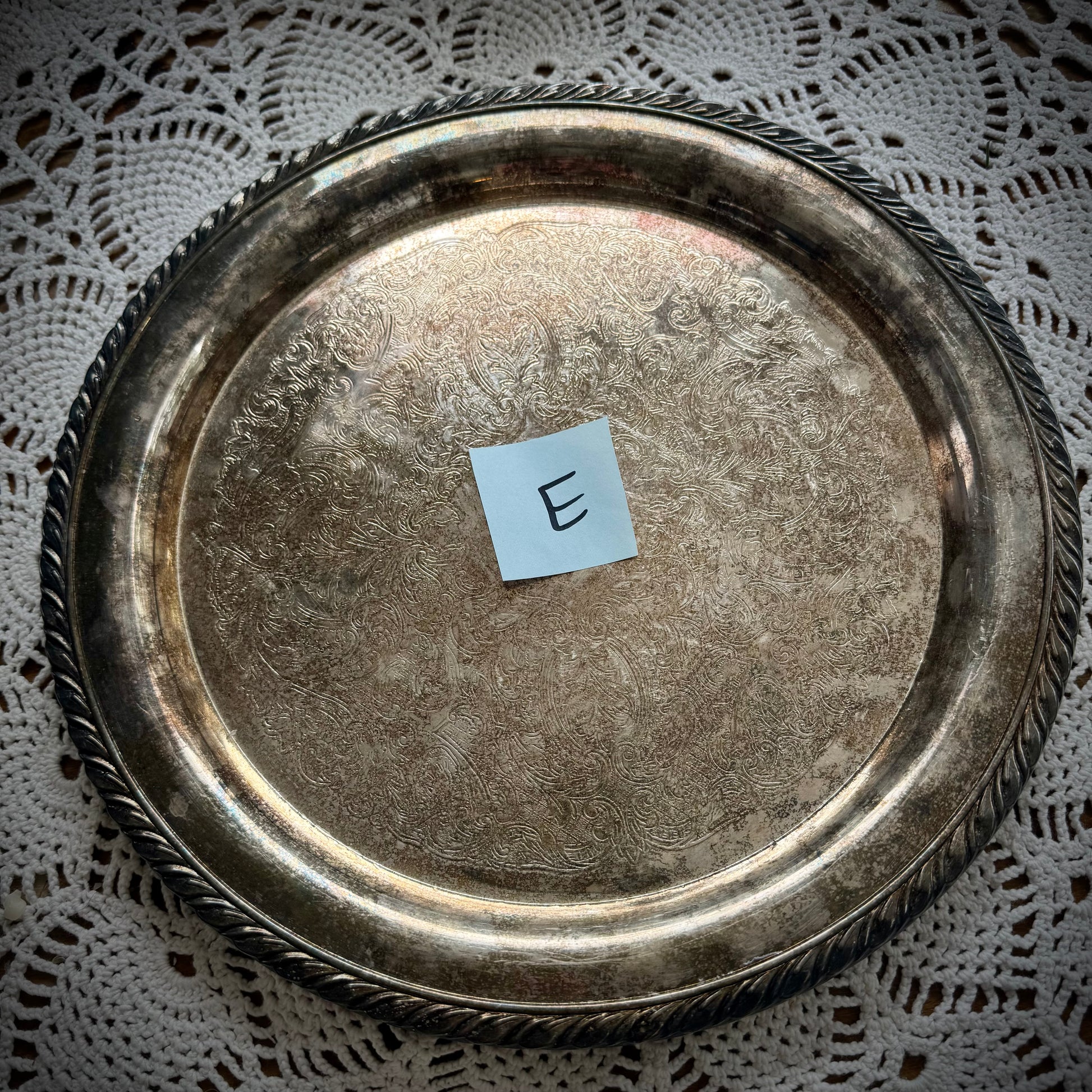 A silverplate round offering tray is displayed on a white lace surface. The tray has a post-it with the letter "E"