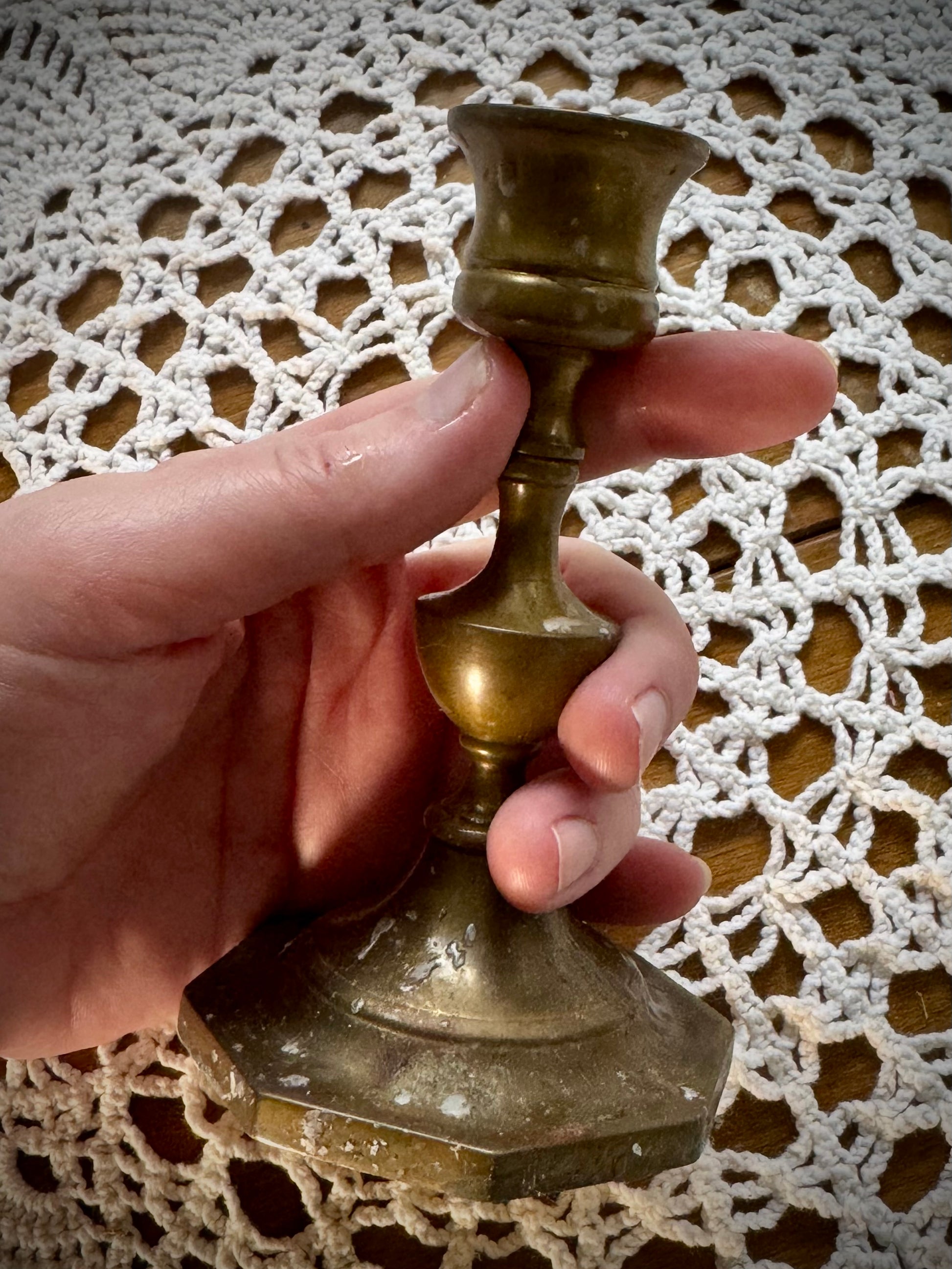 A vintage brass candle holder with an octagonal base, being held over a white lace tablecloth.