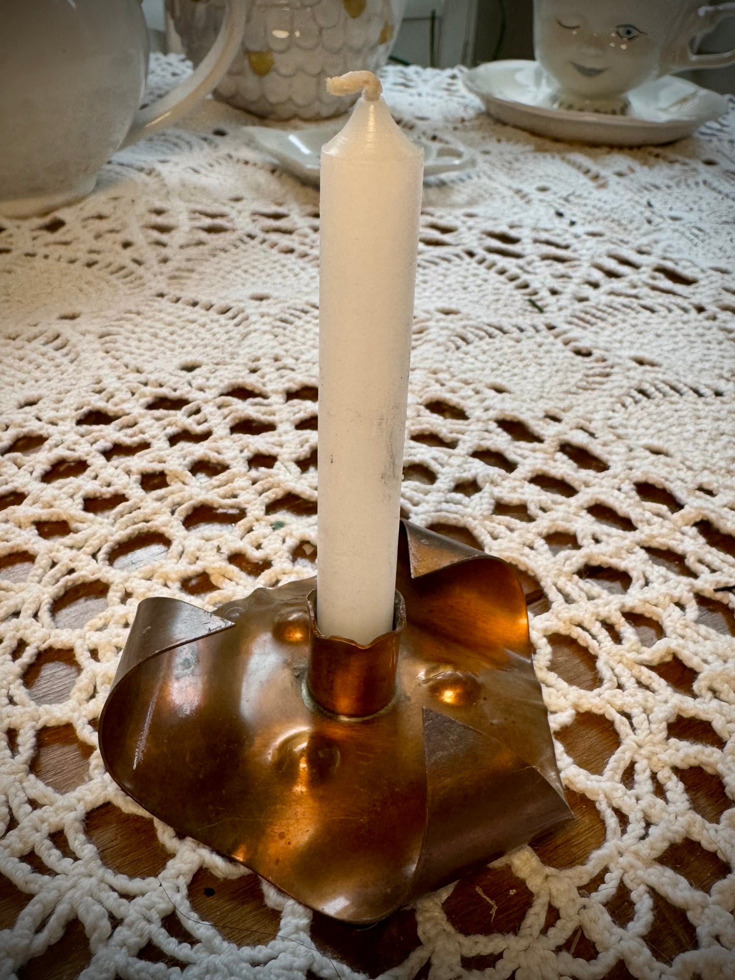 A vintage copper chime candle holder with a white chime candle on a table with a lace tablecloth.