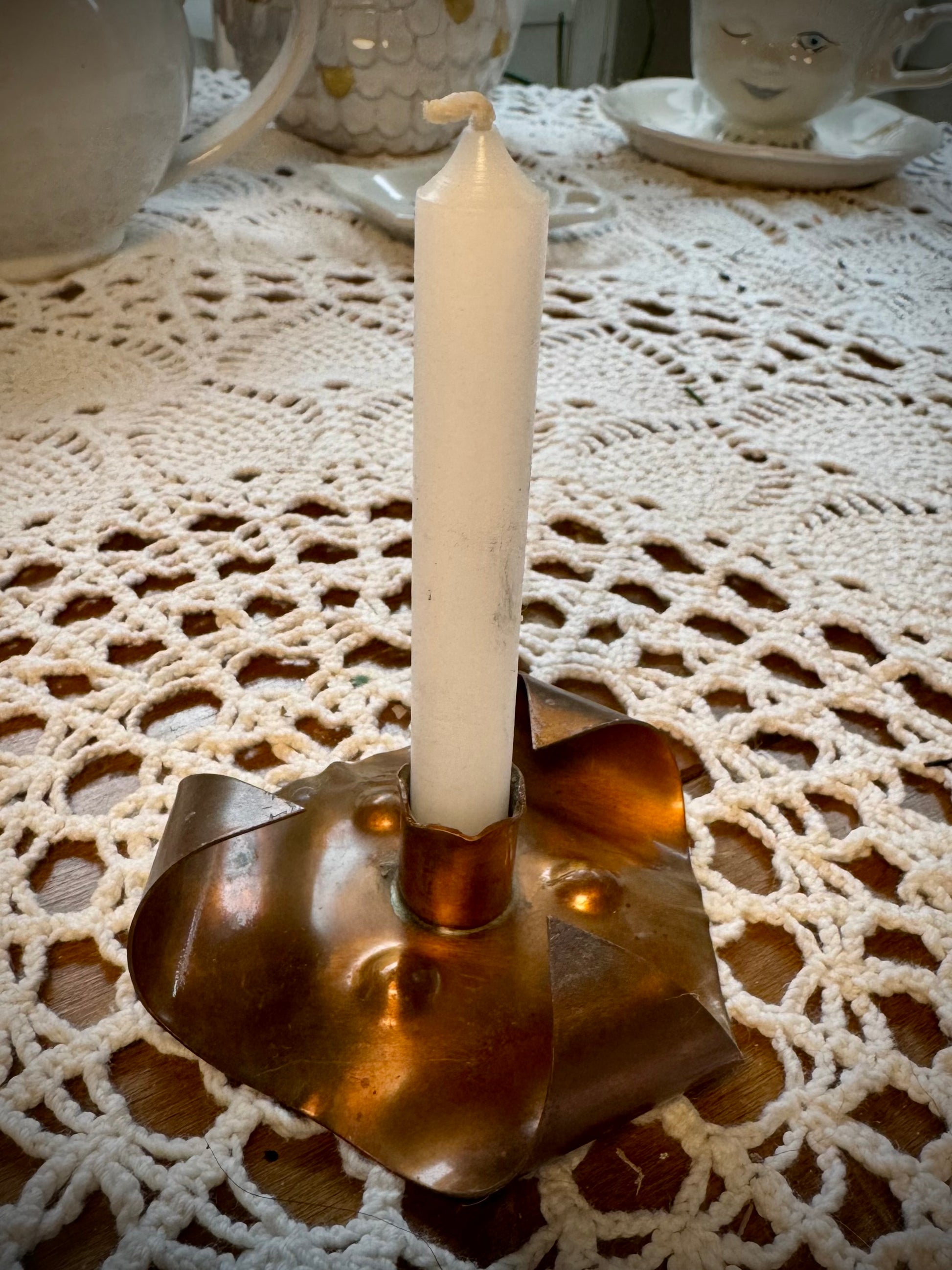 A vintage copper chime candle holder with a white chime candle on a table with a lace tablecloth.