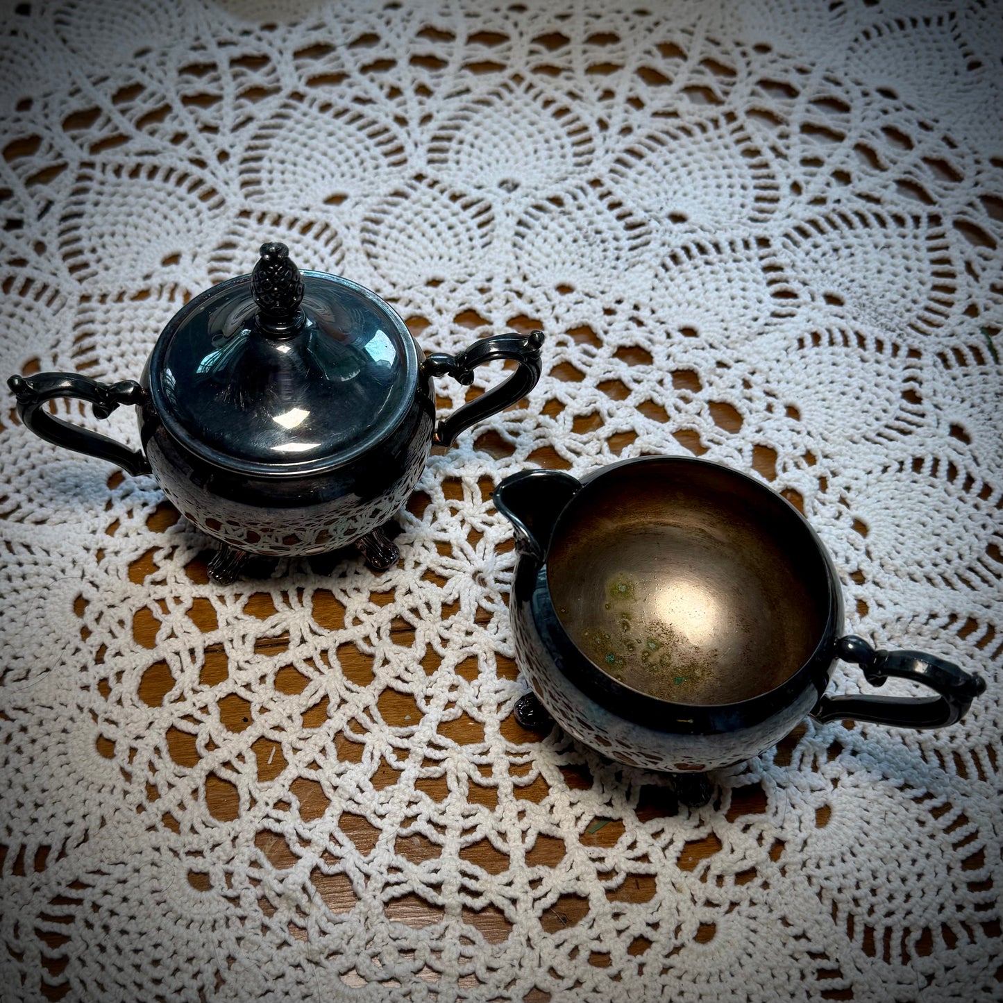 Aerial view of a vintage WM Rogers Silverplate cream and sugar set on a table with a lace tablecloth.