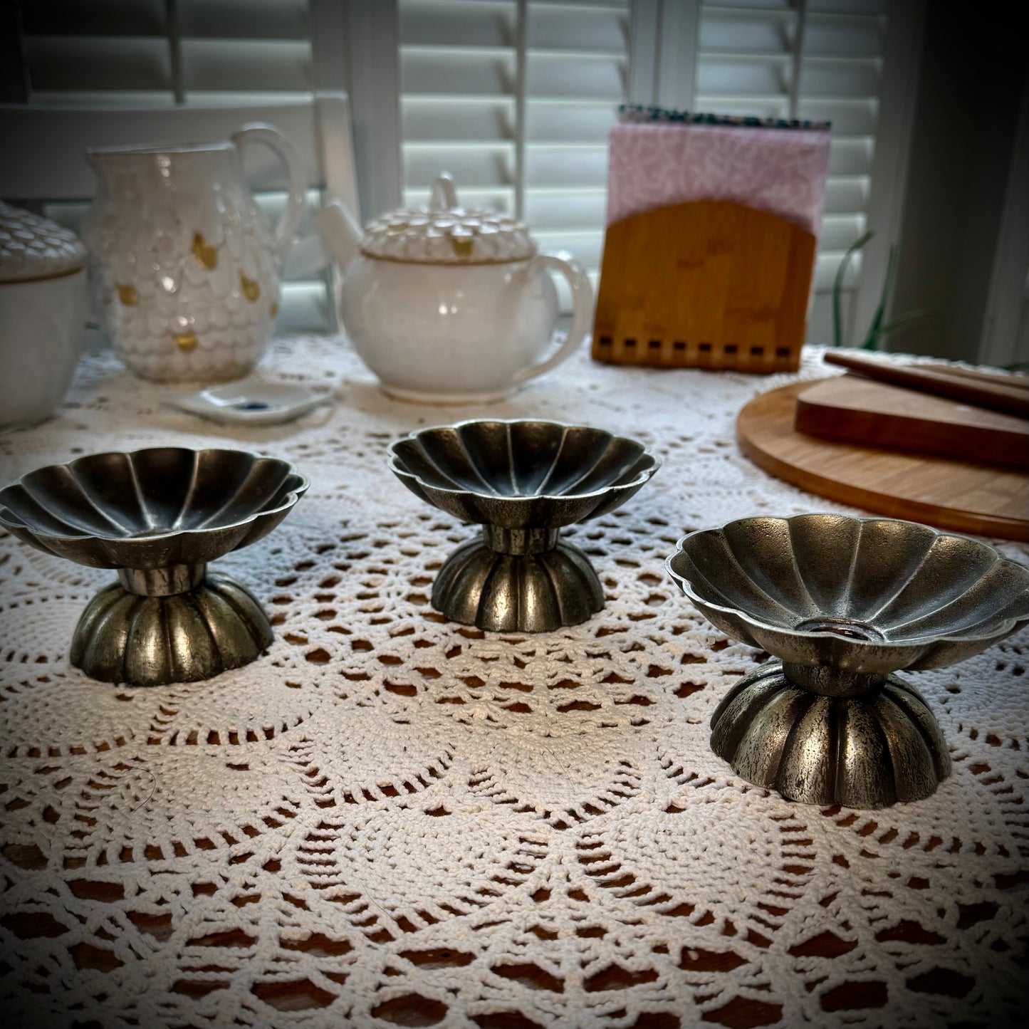 Three vintage pewter swirled taper candle holders displayed on a table with a lace tablecloth.