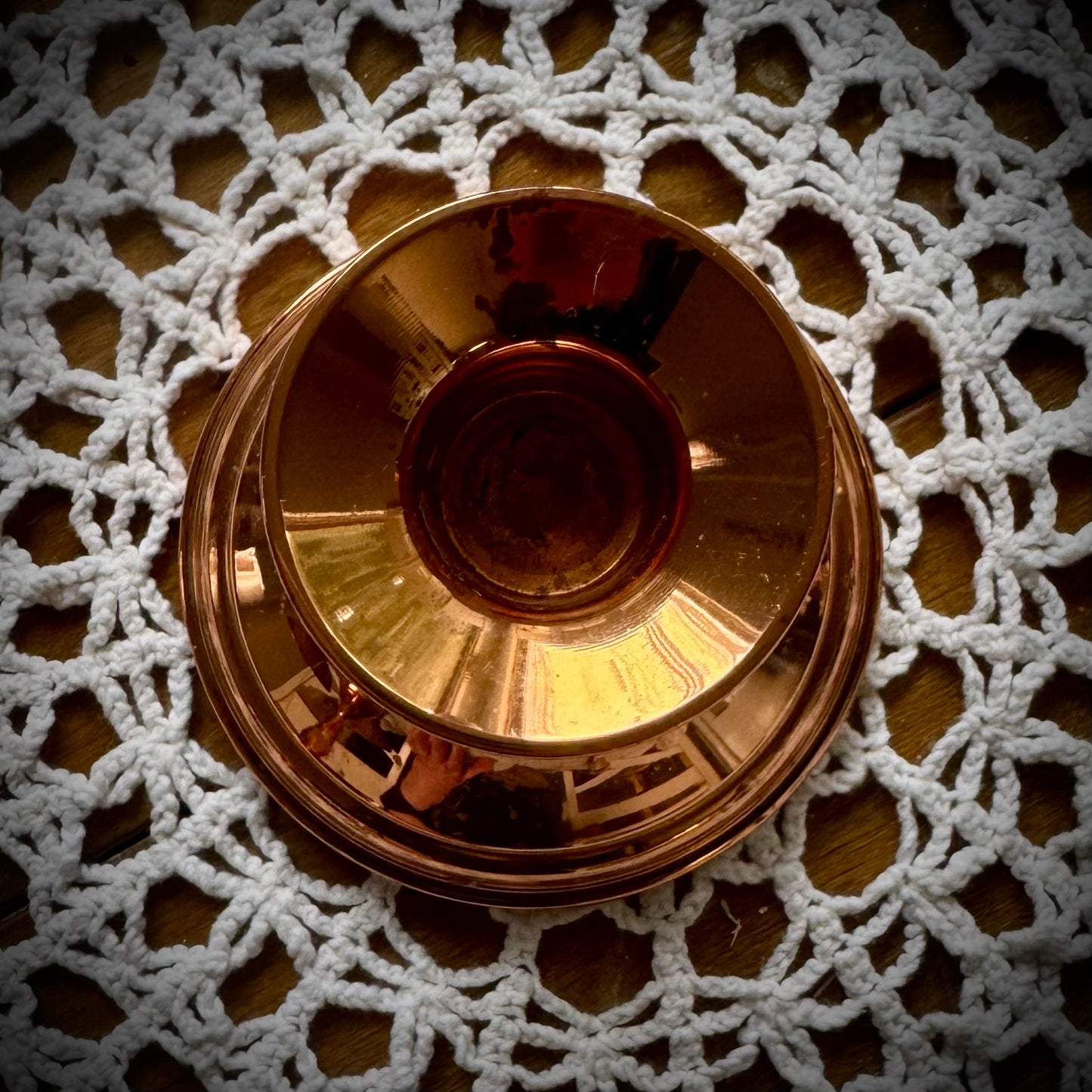 A single vintage copper candle holder displayed on a lace tablecloth.