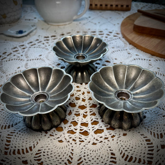 Three vintage pewter swirled taper candle holders displayed on a table with a lace tablecloth.