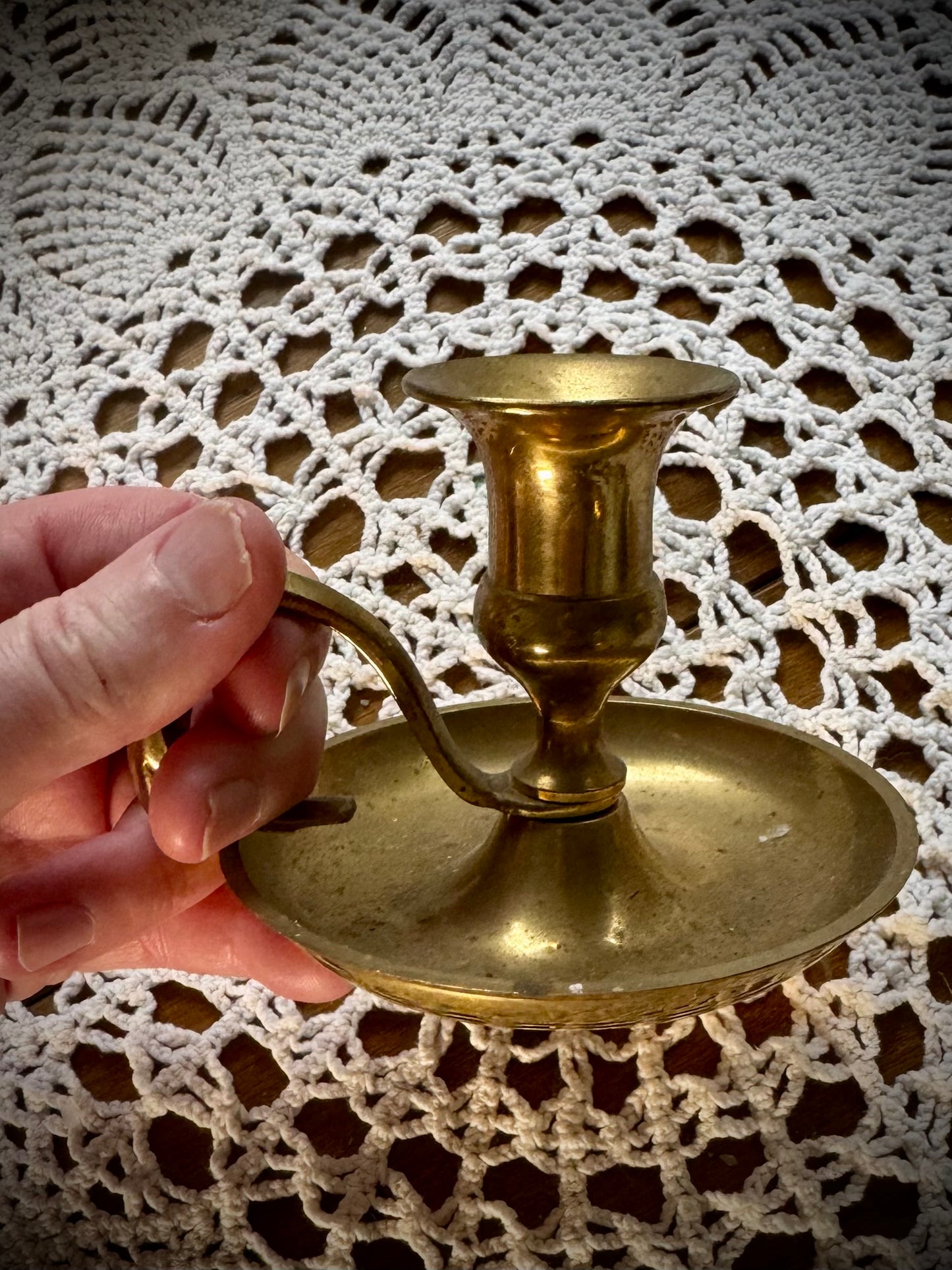 A vintage brass candlestick with a finger loop on a table with a lace tablecloth.