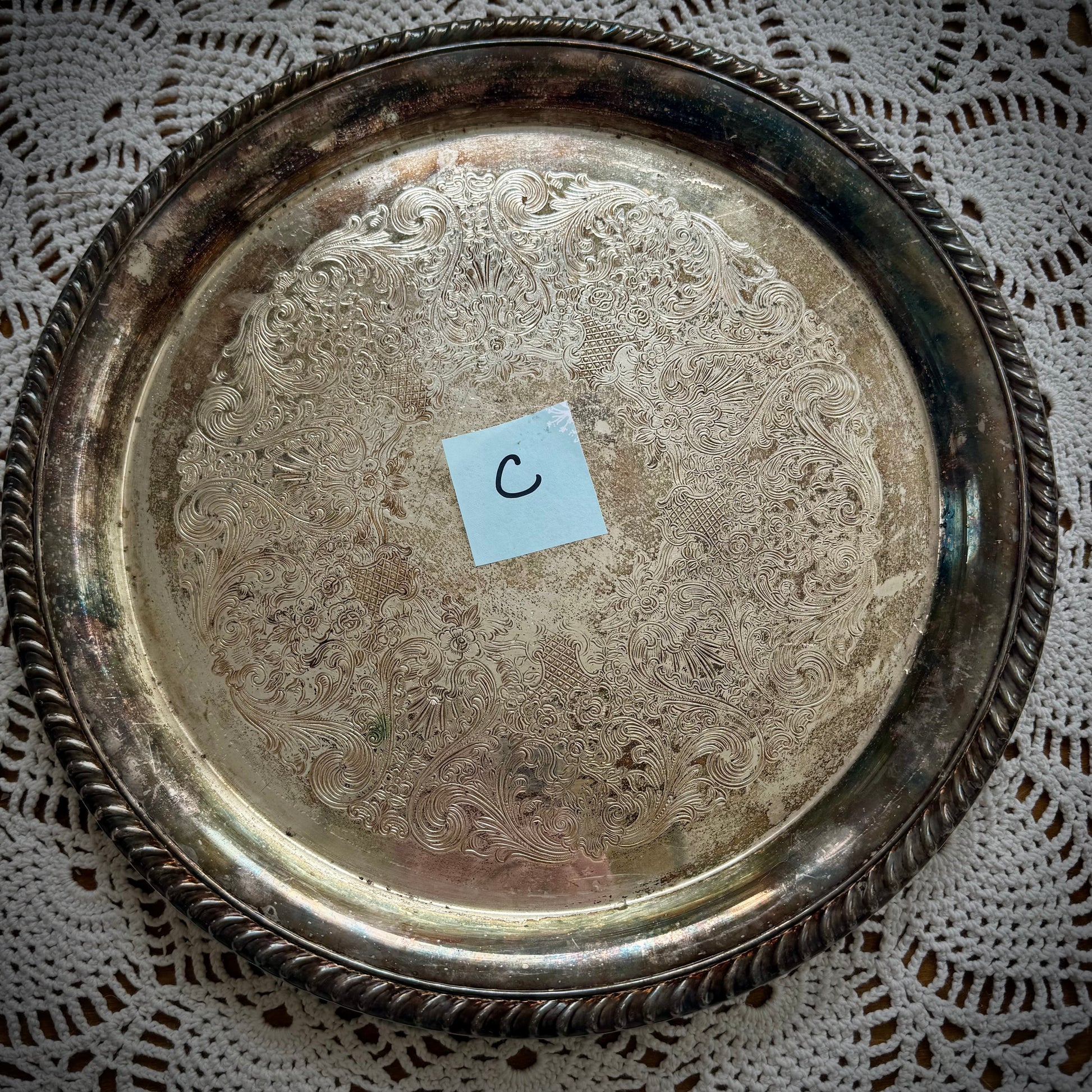 A silverplate round offering tray is displayed on a white lace surface. The tray has a post-it with the letter "C"