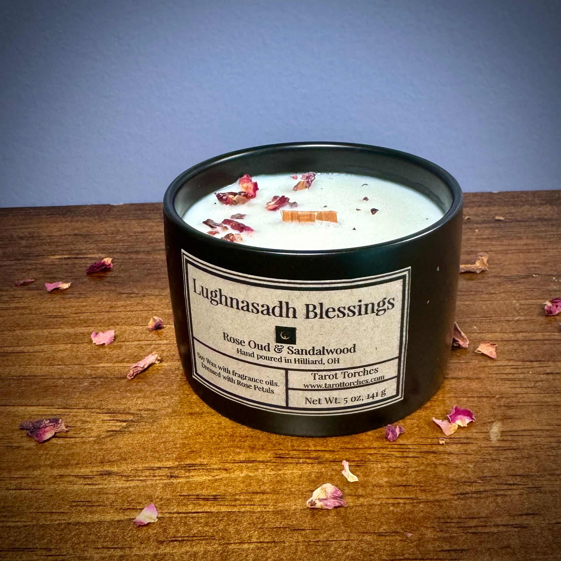 A ceramic candle labeled 'Lughnasadh Blessings' placed on a wooden surface against a purple background.