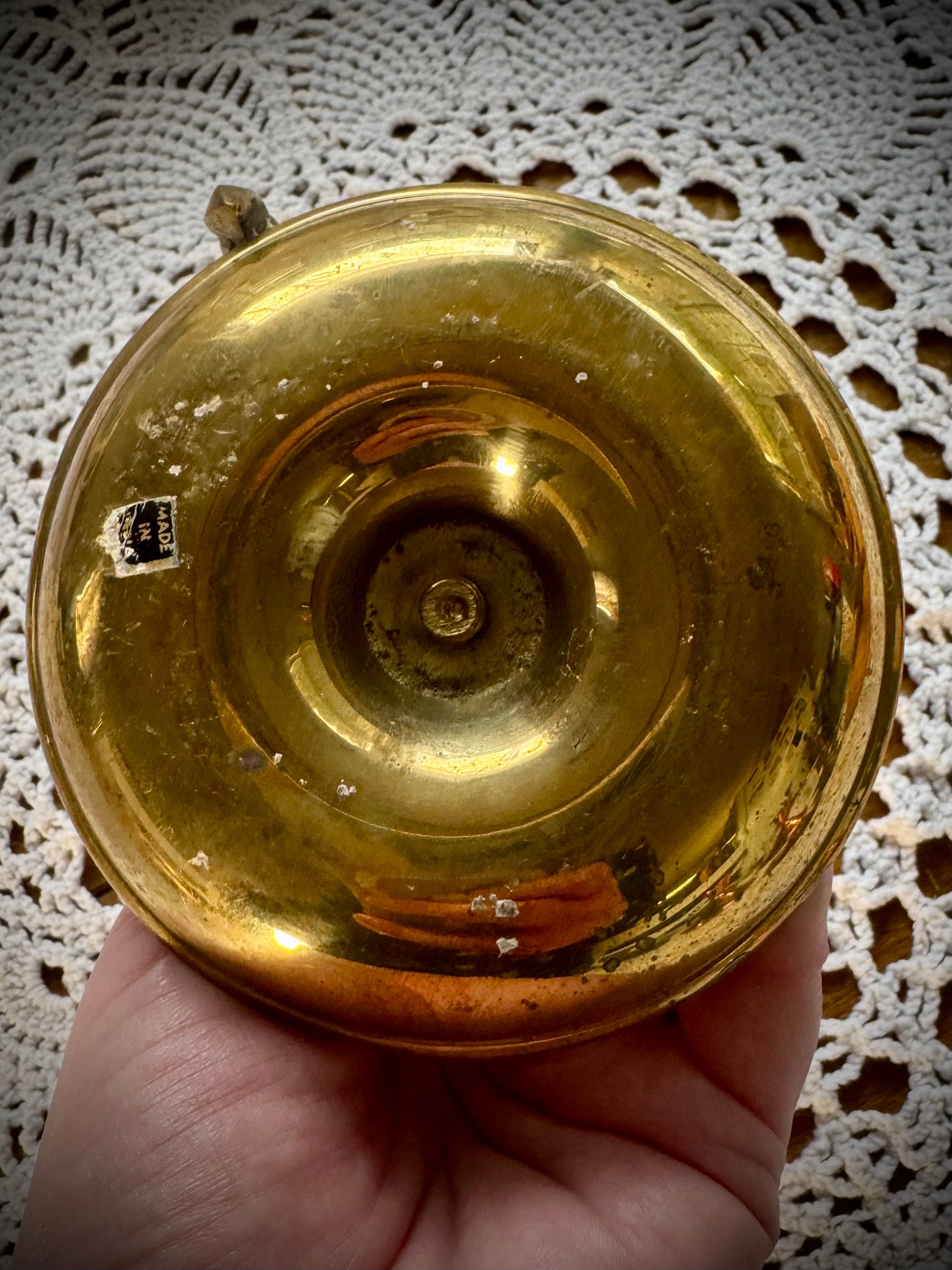 Bottom view of a vintage brass candlestick with a finger loop on a table with a lace tablecloth.