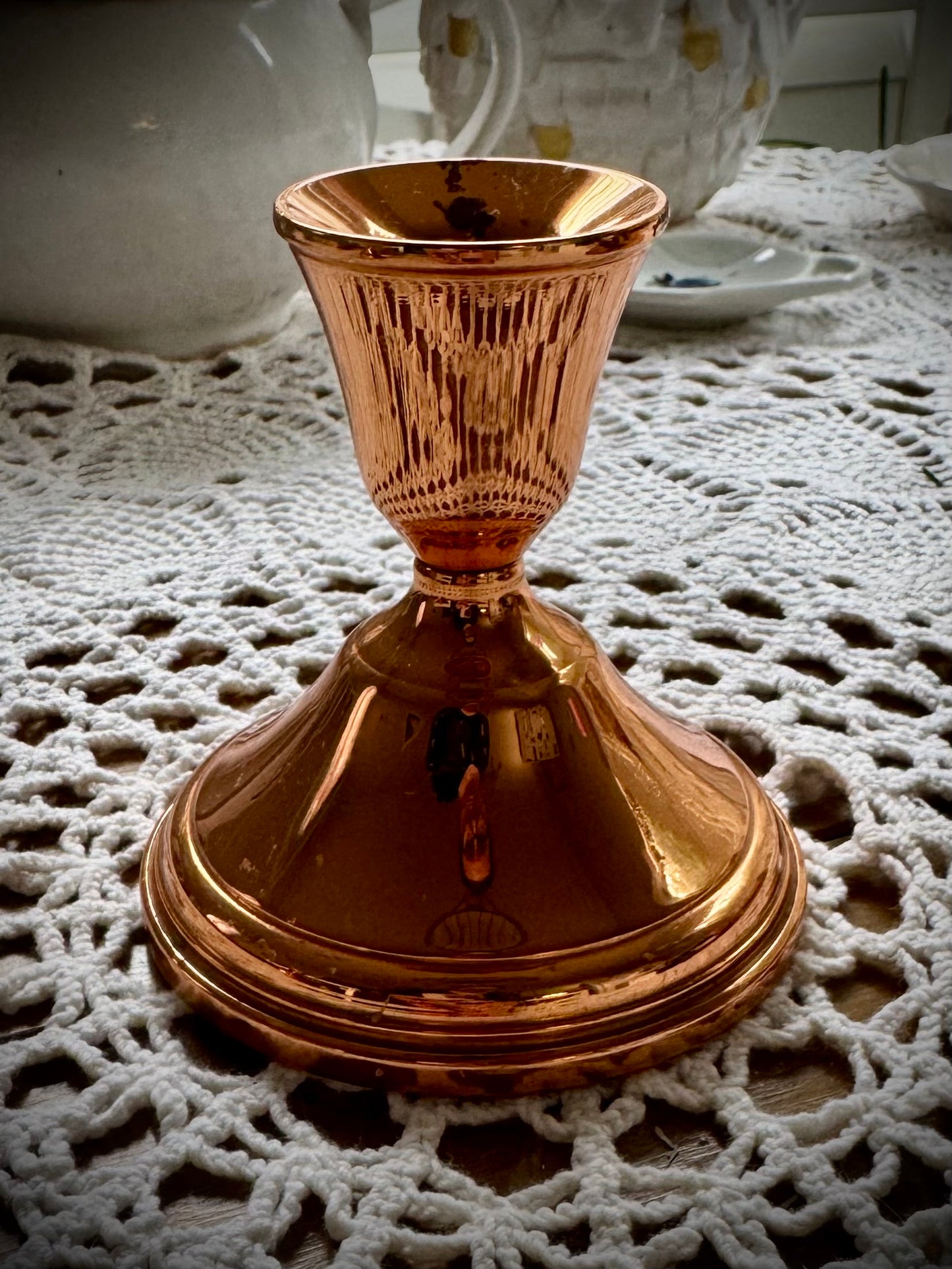 A single vintage copper candle holder displayed on a lace tablecloth.
