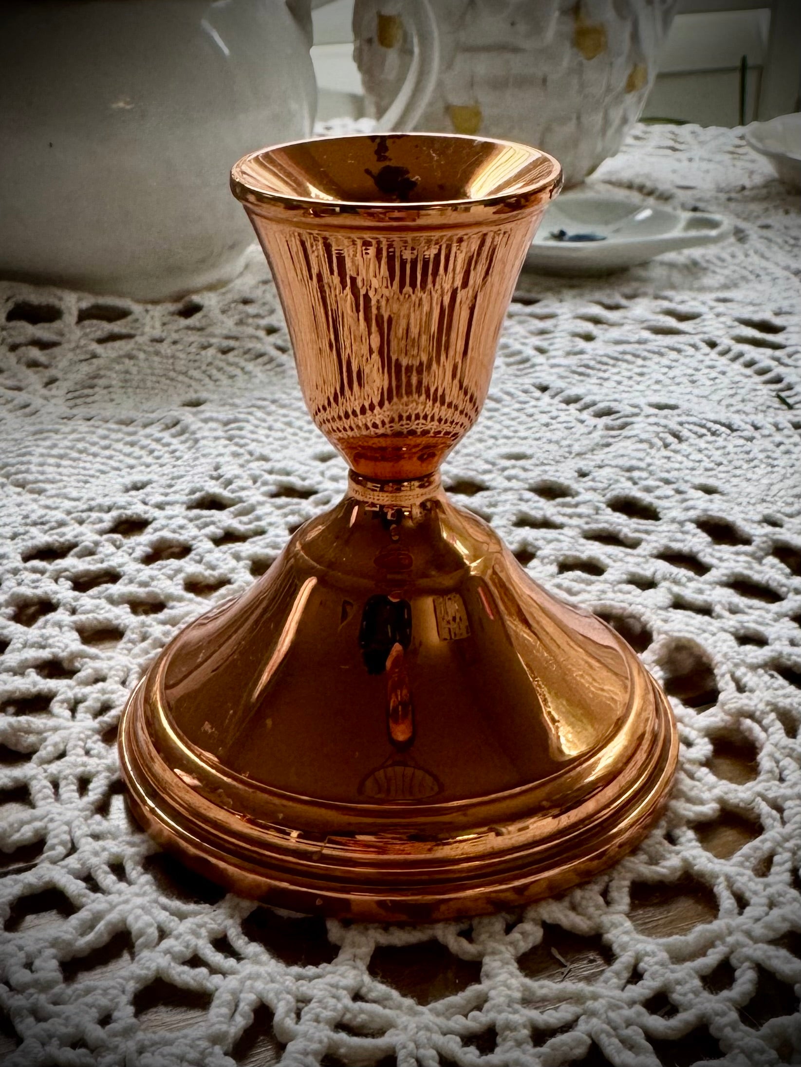 A single vintage copper candle holder displayed on a lace tablecloth.