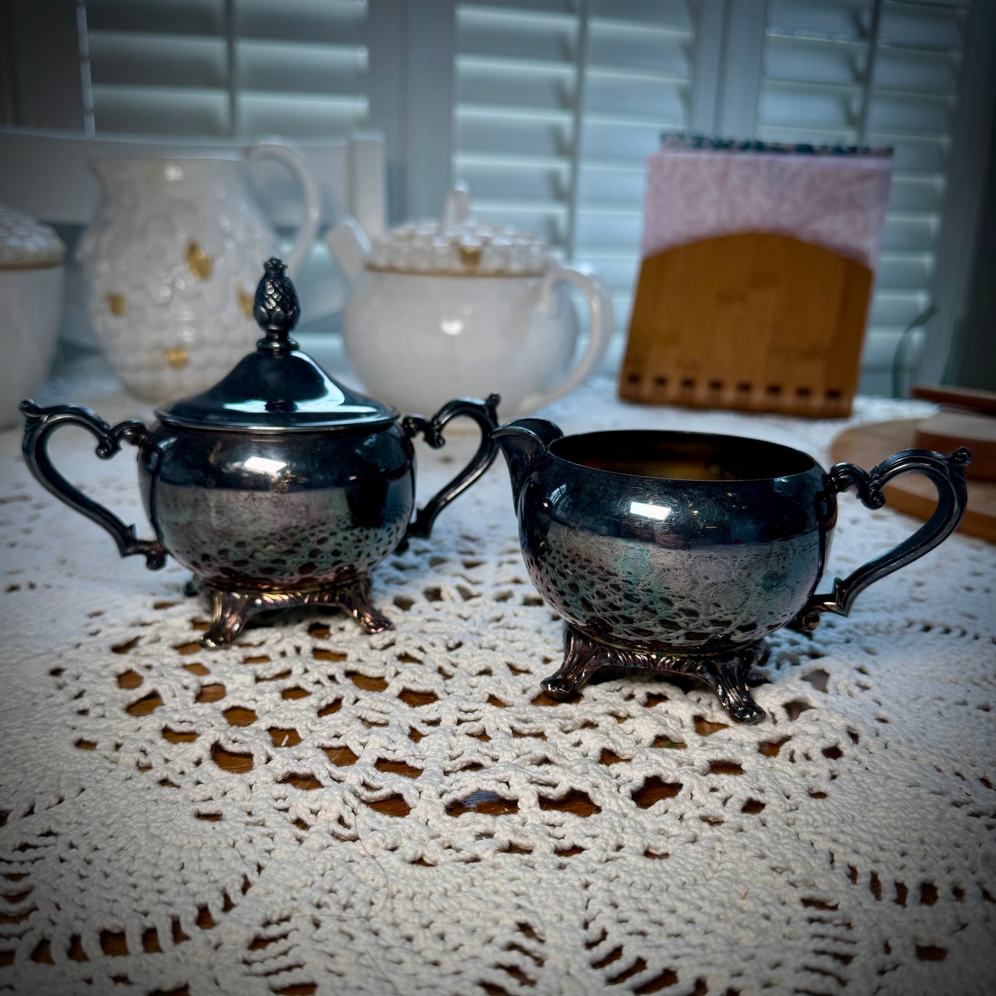 A vintage WM Rogers Silverplate cream and sugar set on a table with a lace tablecloth.