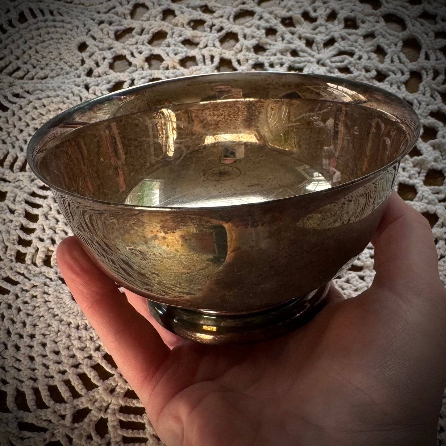 A silver plate altar bowl with a patterned exterior, placed on a white lace surface.