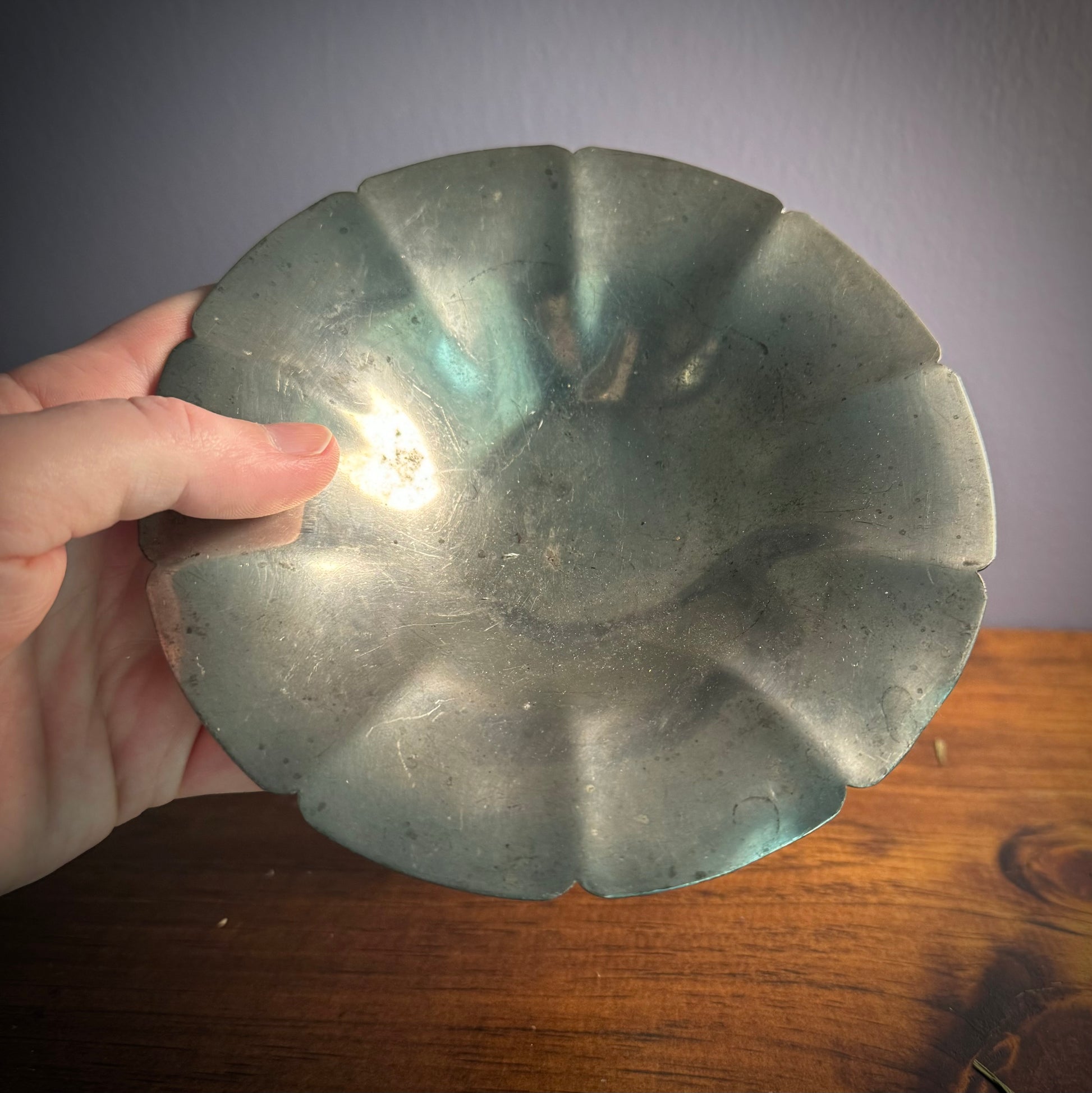 A silver pewter bowl being held over a wooden surface with a plain blue background.