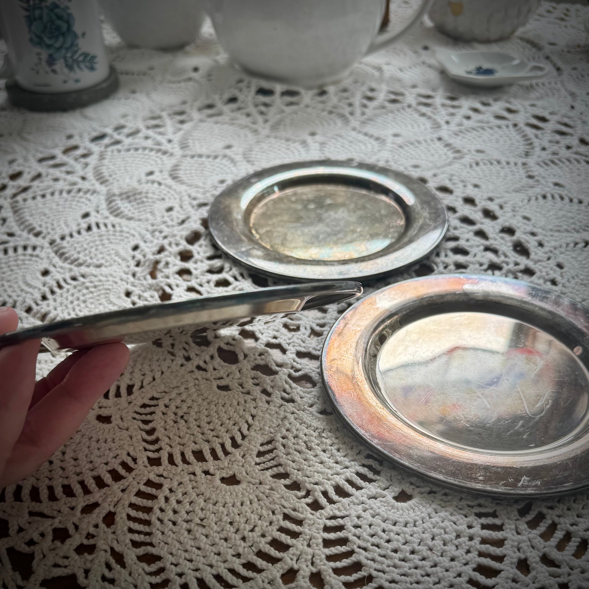 Three round silverplate Offering Plates on a lace surface, reflecting light and showing signs of wear.