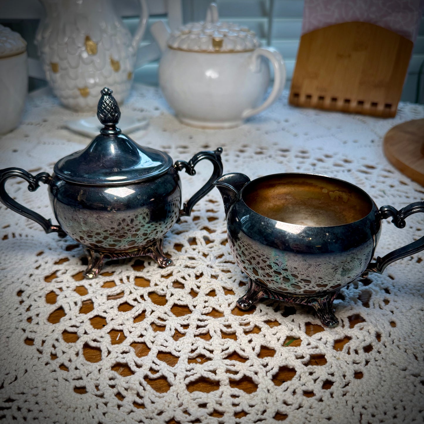 A vintage WM Rogers Silverplate cream and sugar set on a table with a lace tablecloth.