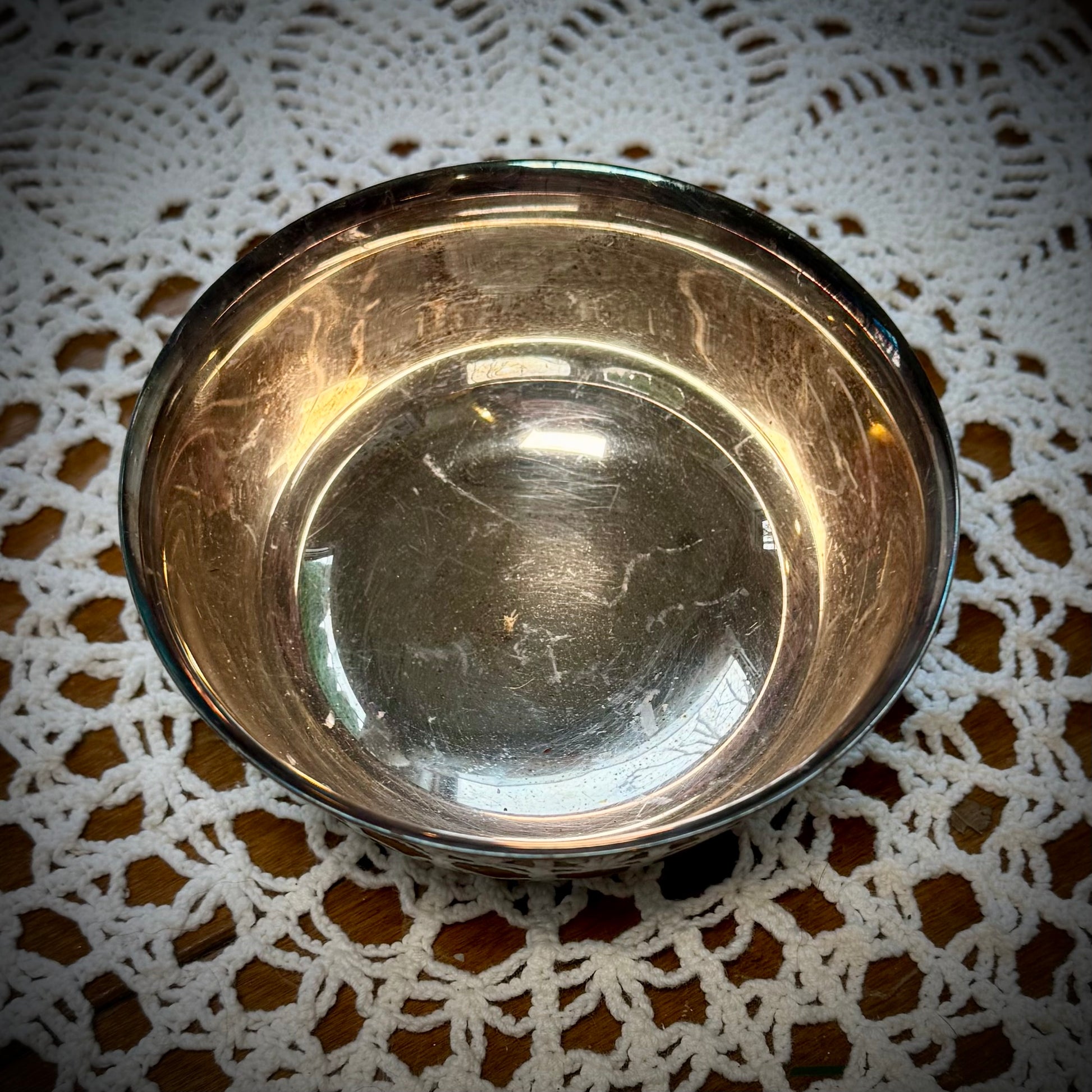 A silver plate altar bowl with a patterned exterior, placed on a white lace surface.