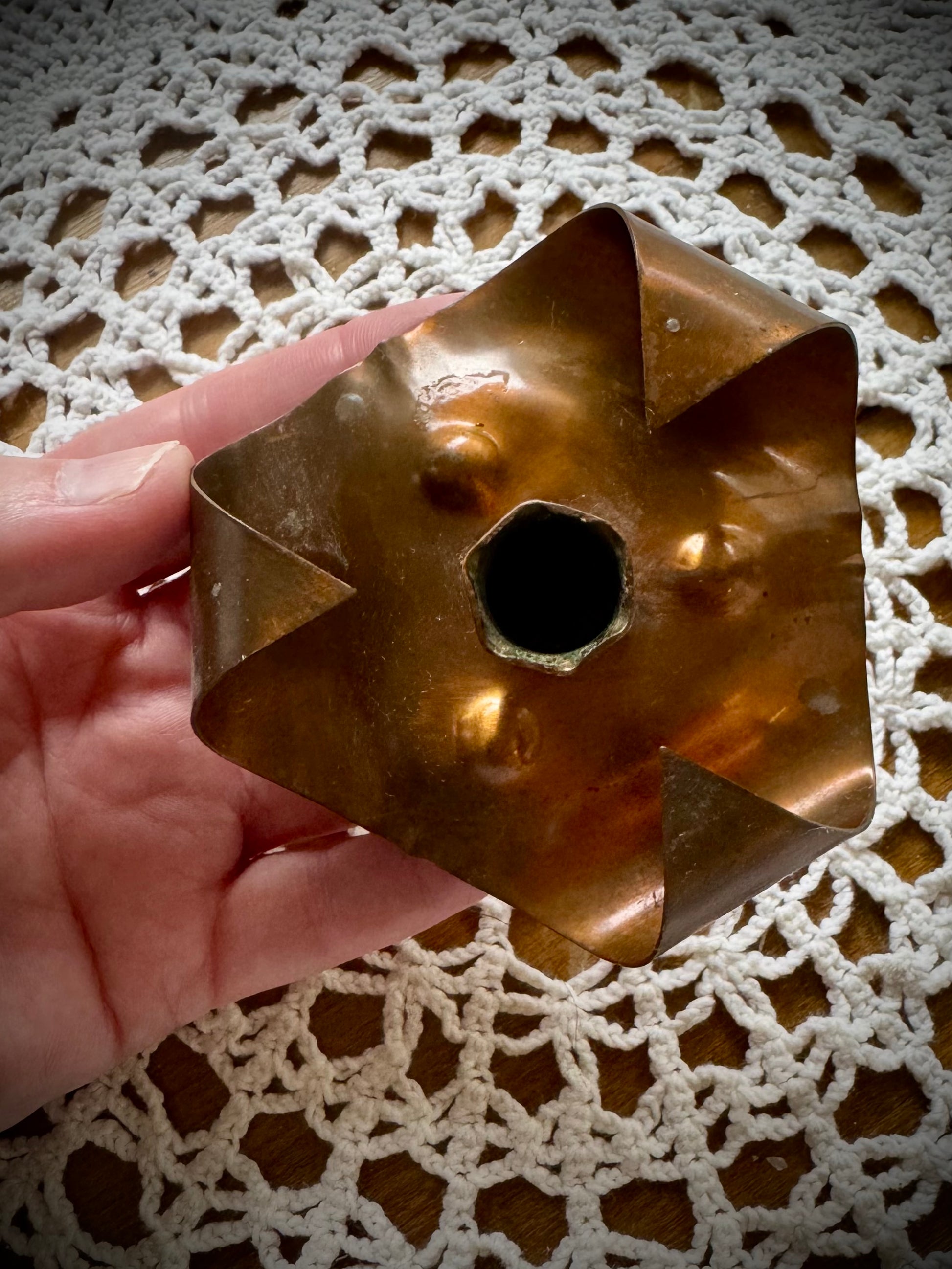 A vintage copper chime candle holder on a table with a lace tablecloth.