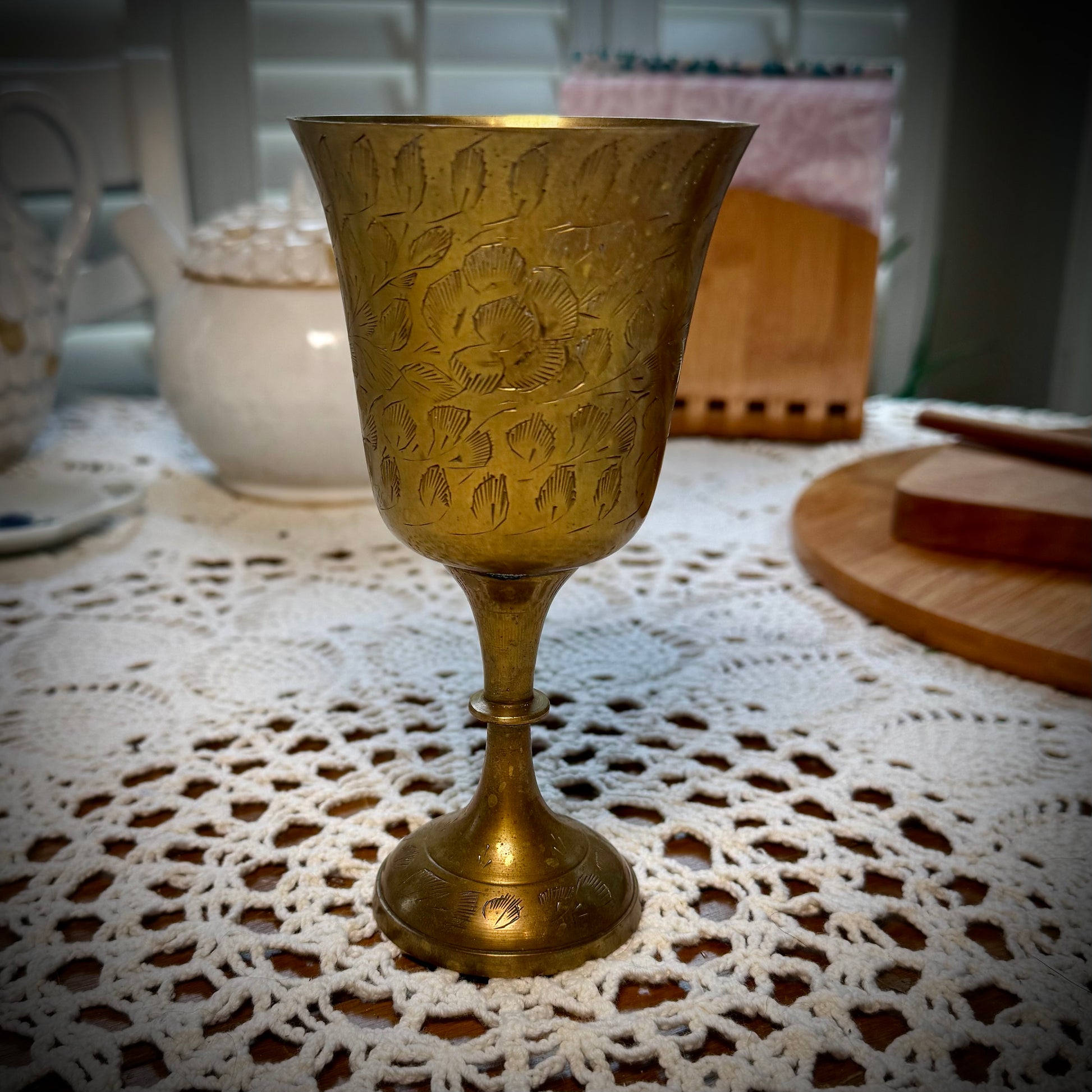 Etched brass colored goblet placed on a table with a white lace tablecloth