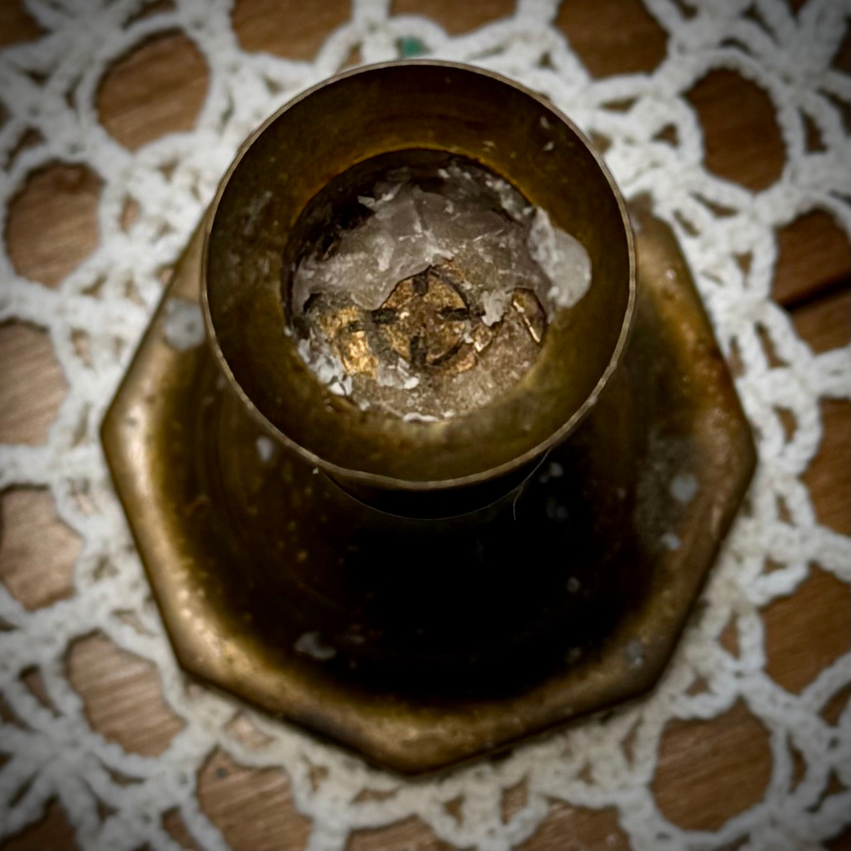A vintage brass candle holder with an octagonal base, placed on a lace tablecloth.