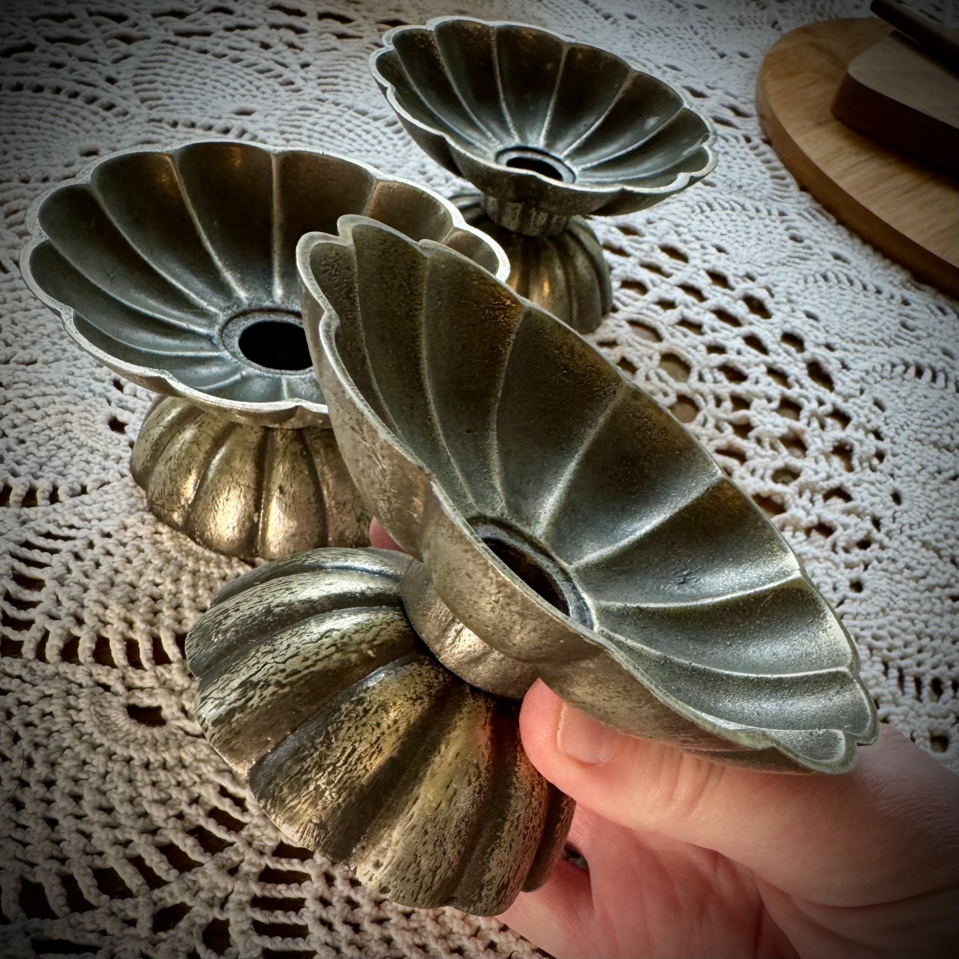 Three vintage pewter swirled taper candle holders, one being held to show the side view.