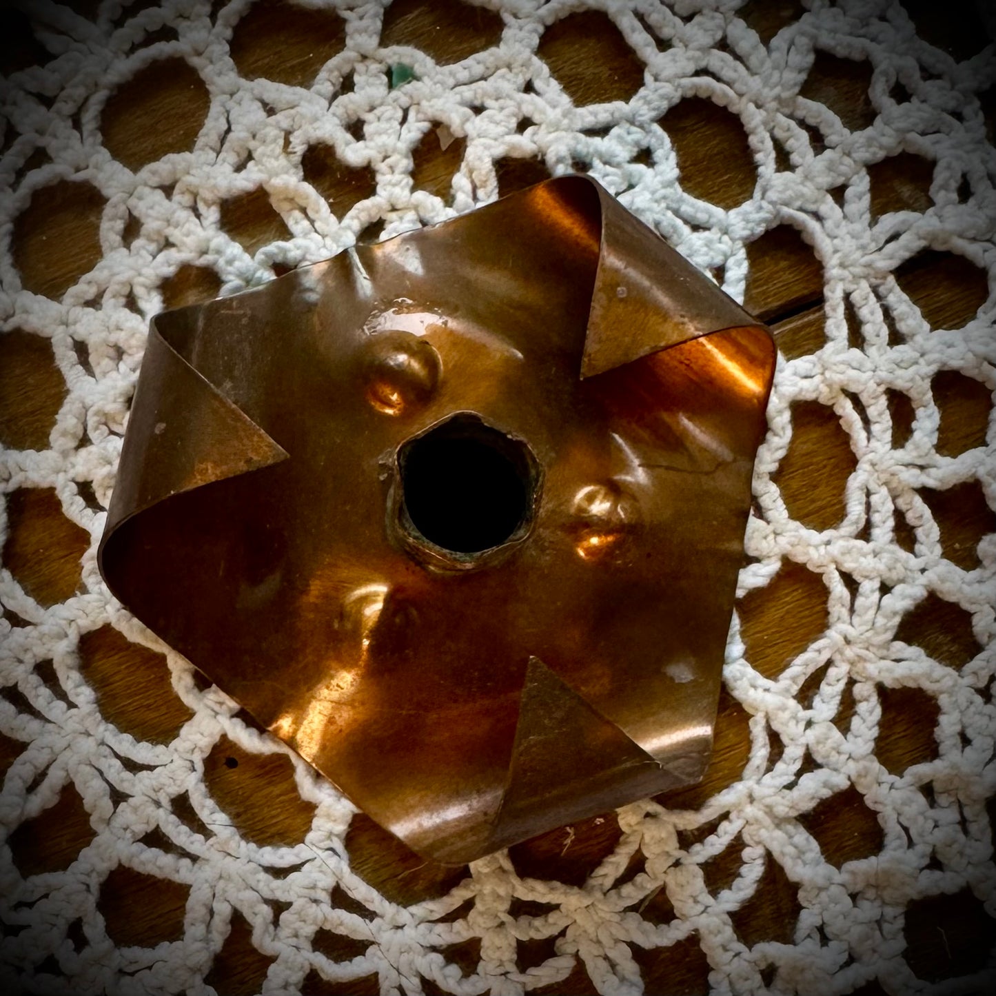 A vintage copper chime candle holder on a table with a lace tablecloth.