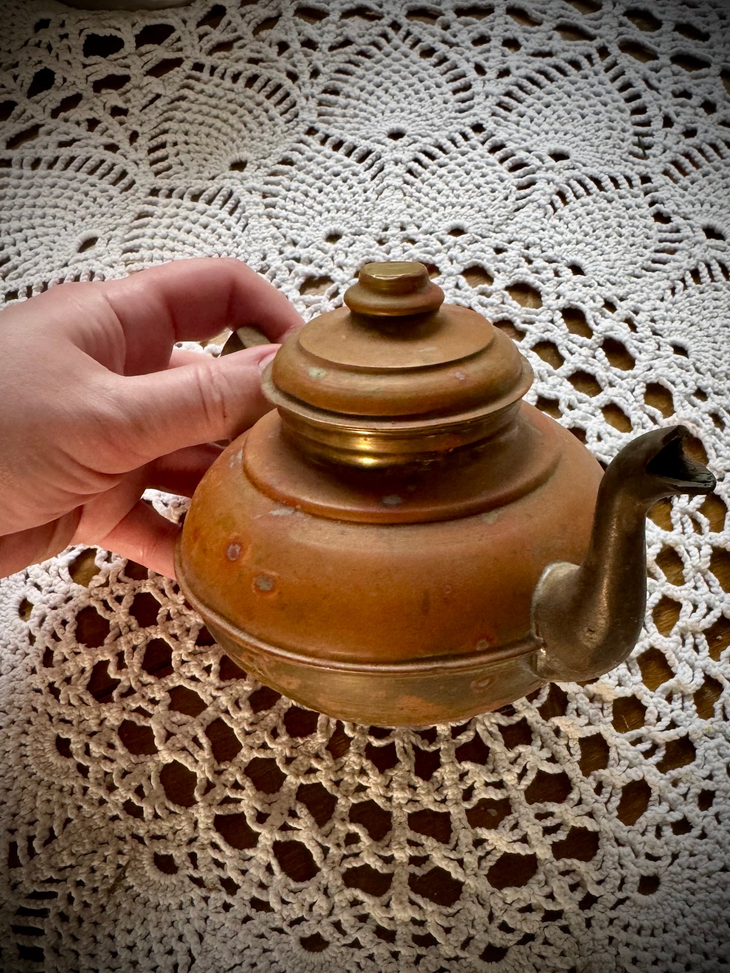 A vintage copper teapot with a Middle Eastern style design, placed on a table with a white lace tablecloth.
