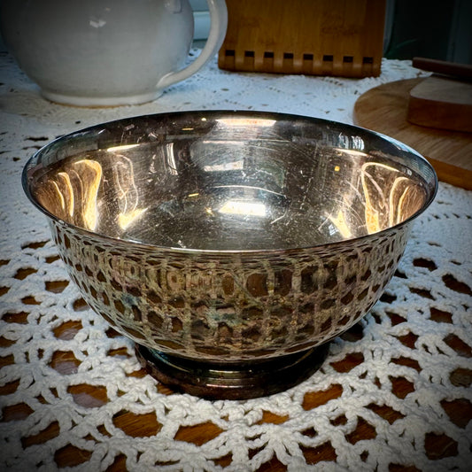 A silver plate altar bowl with a patterned exterior, placed on a white lace surface.