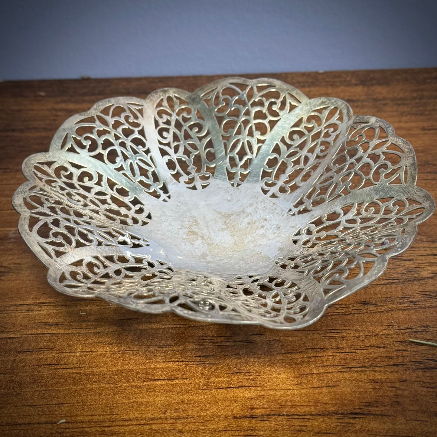 A vintage silver ritual plate with intricate floral lace patterns on a wooden surface.