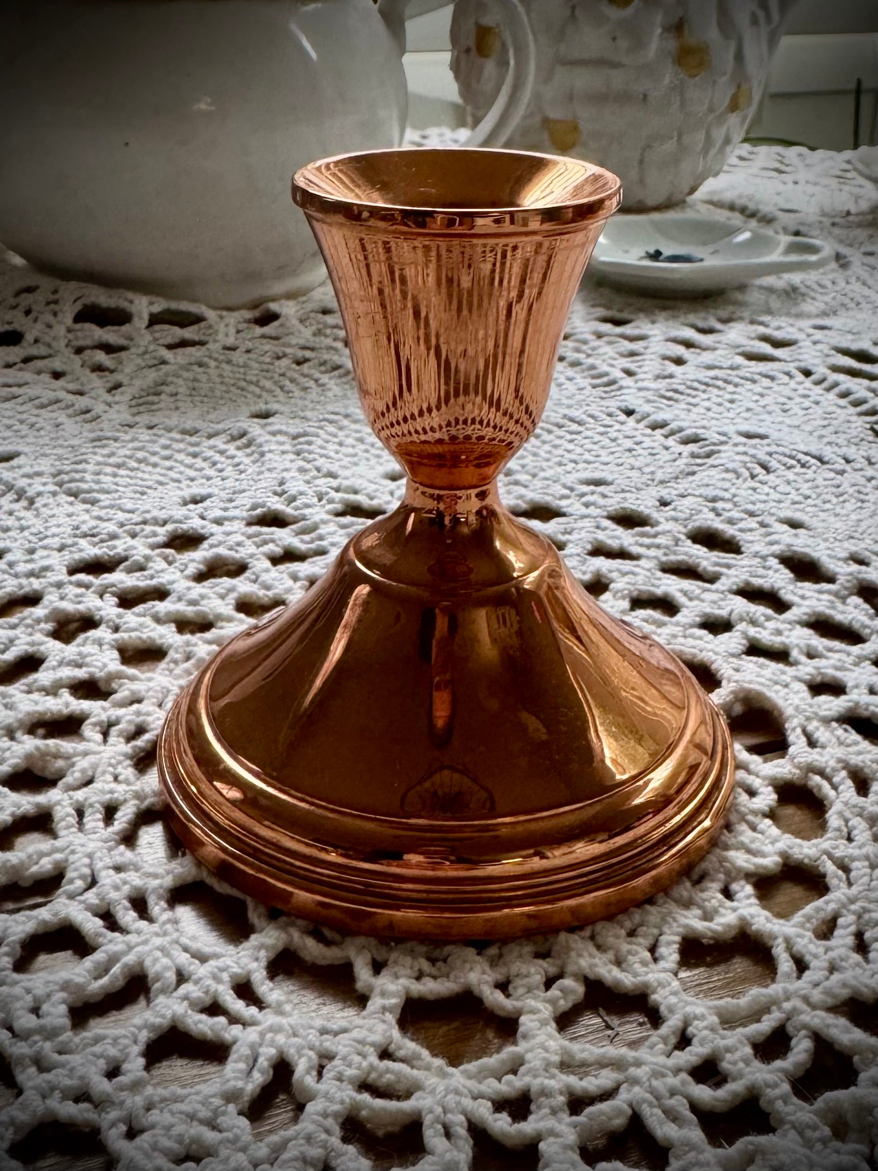 A single vintage copper candle holder displayed on a lace tablecloth.